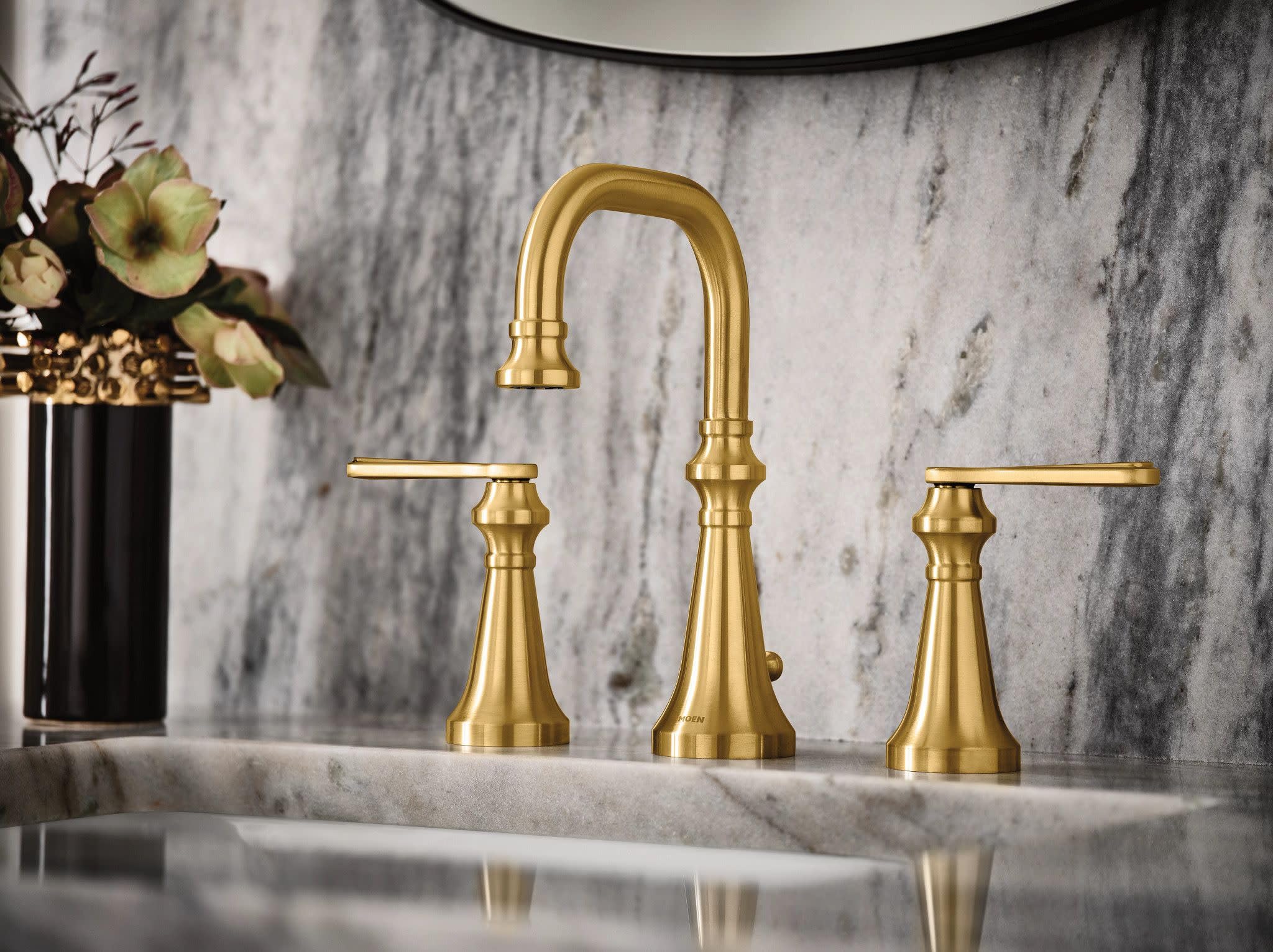 Brushed gold two-handle bathroom faucet with curved center spout and tapered base handles on marble countertop.