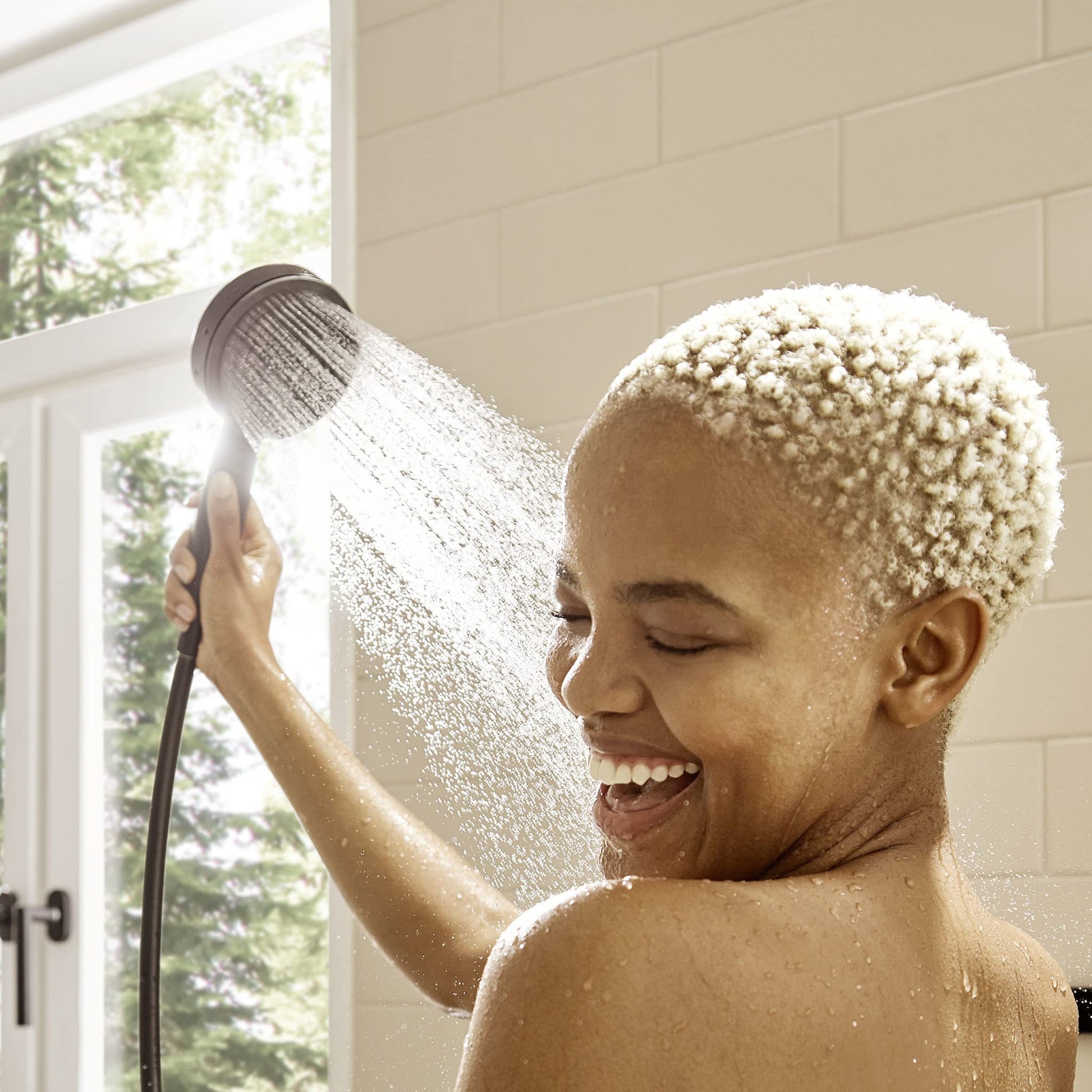 Matte black wall-mounted shower head with hose dispensing water in a bathroom with cream subway tile walls.