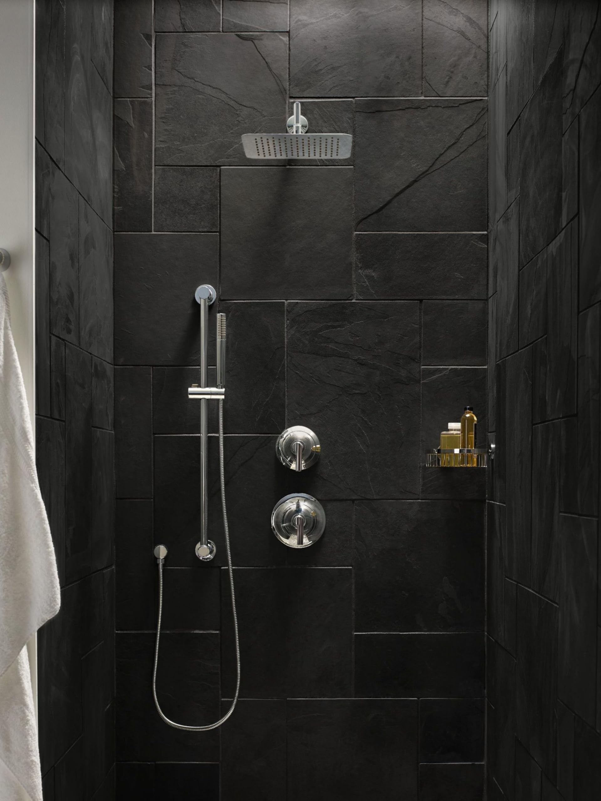 Chrome handheld shower system with slide bar, metal hose, and overhead rainfall showerhead installed on dark tile shower wall