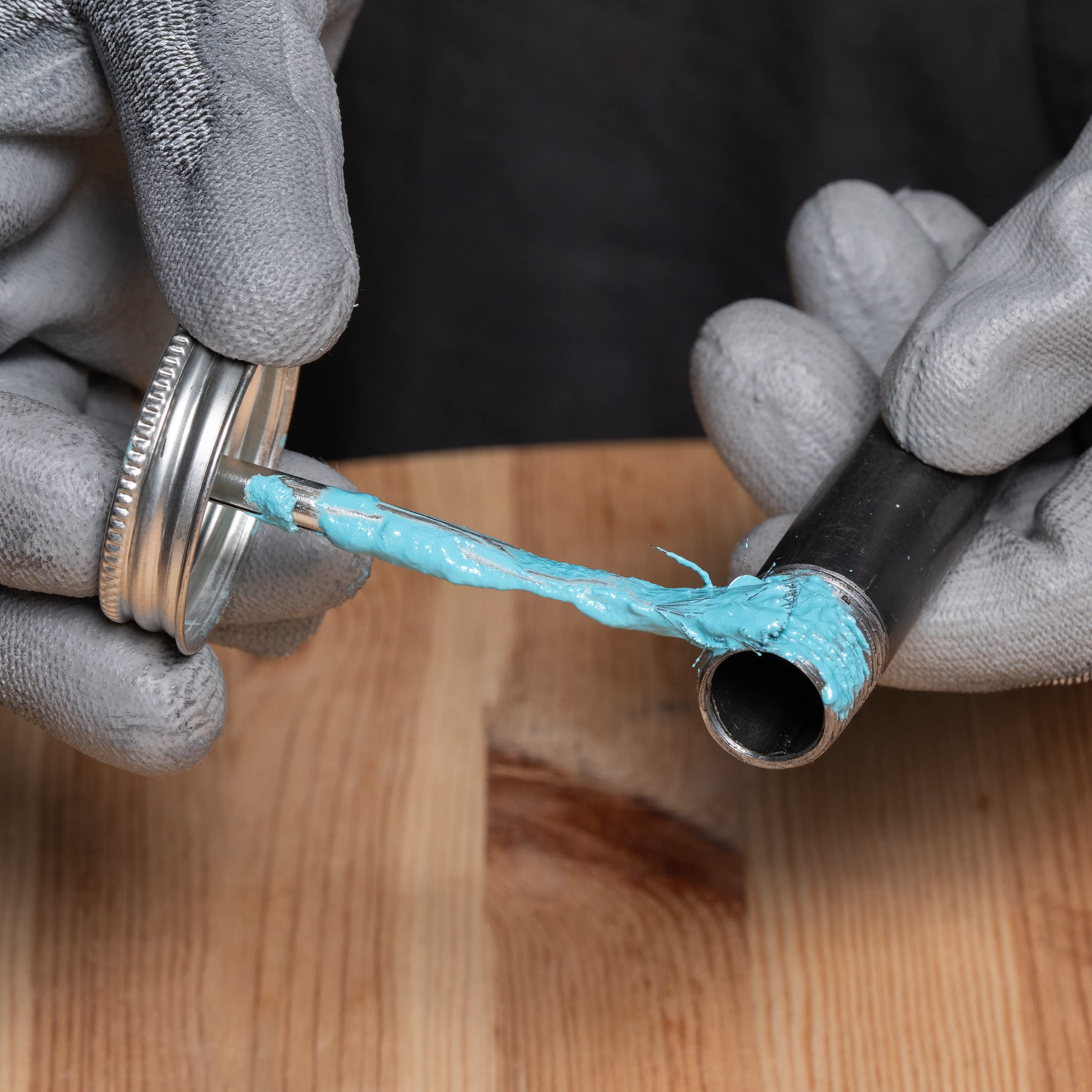 Blue pipe joint compound being applied to a metal pipe fitting with a applicator brush.