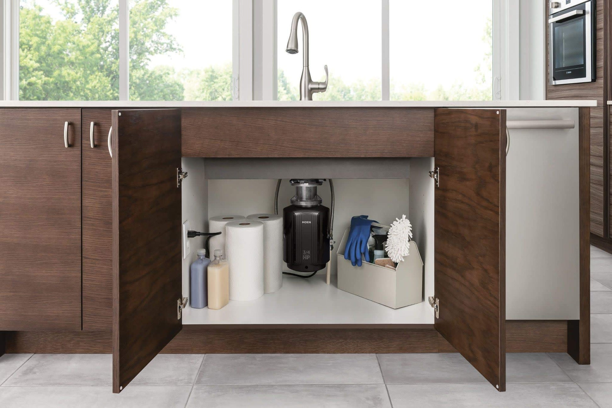 Black cylindrical garbage disposal unit installed under kitchen sink cabinet with power cord visible.