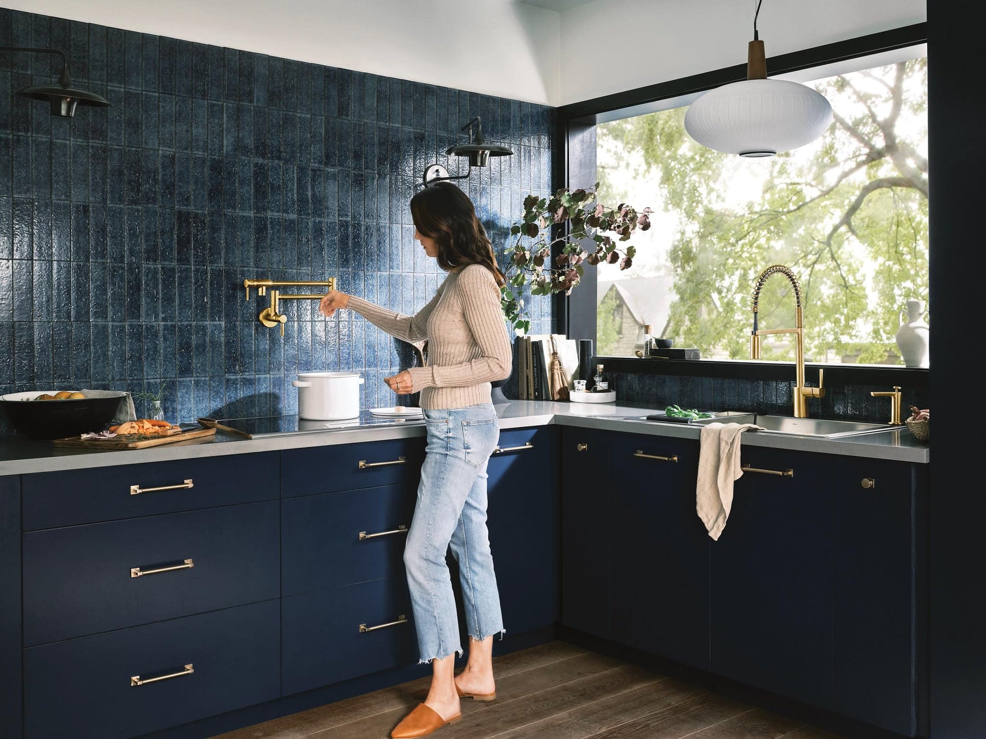 Brushed gold wall-mounted pot filler faucet with double-jointed folding swing arm installed above kitchen stovetop.