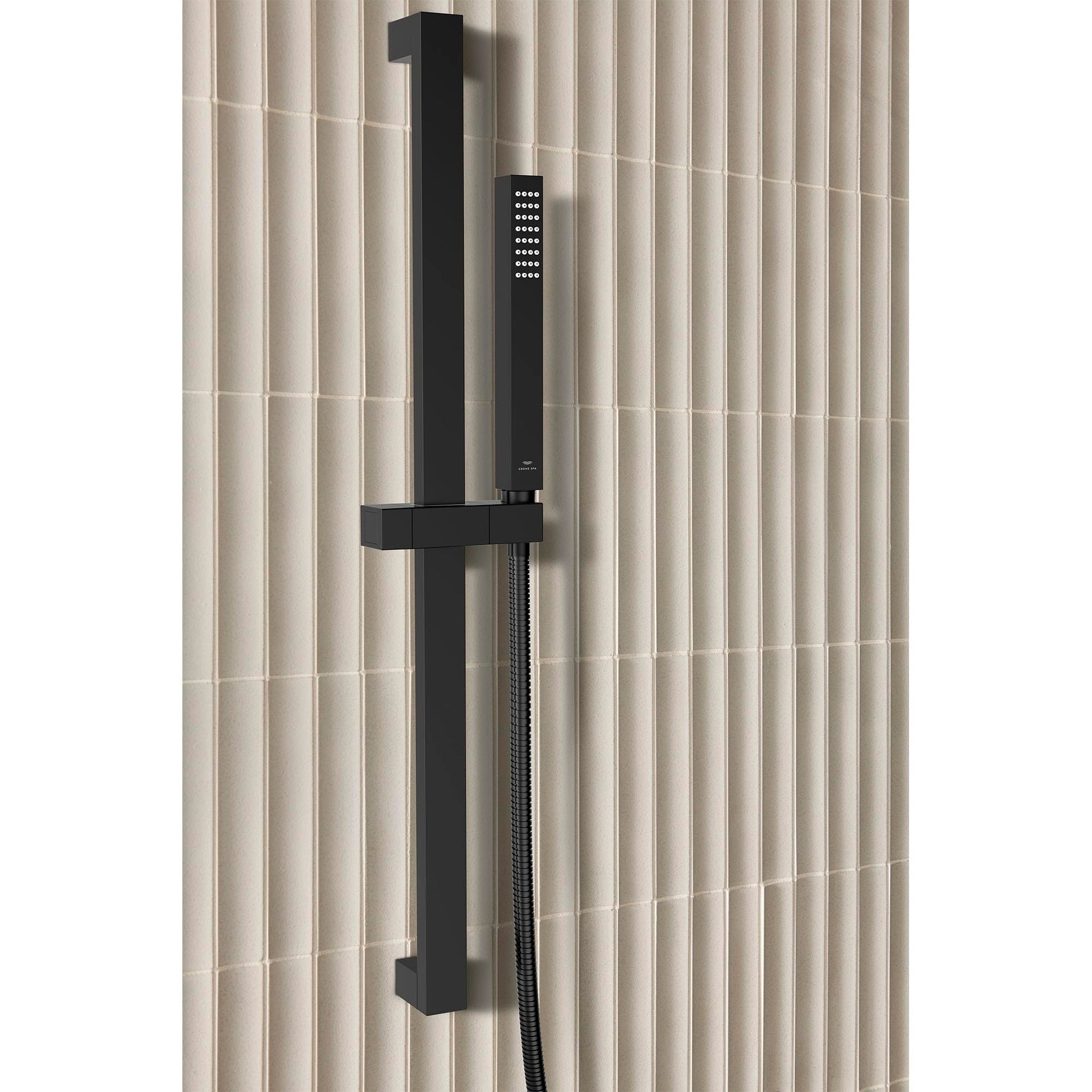 Matte black rectangular hand shower with cube-shaped head mounted on vertical rail with hose against tiled wall.