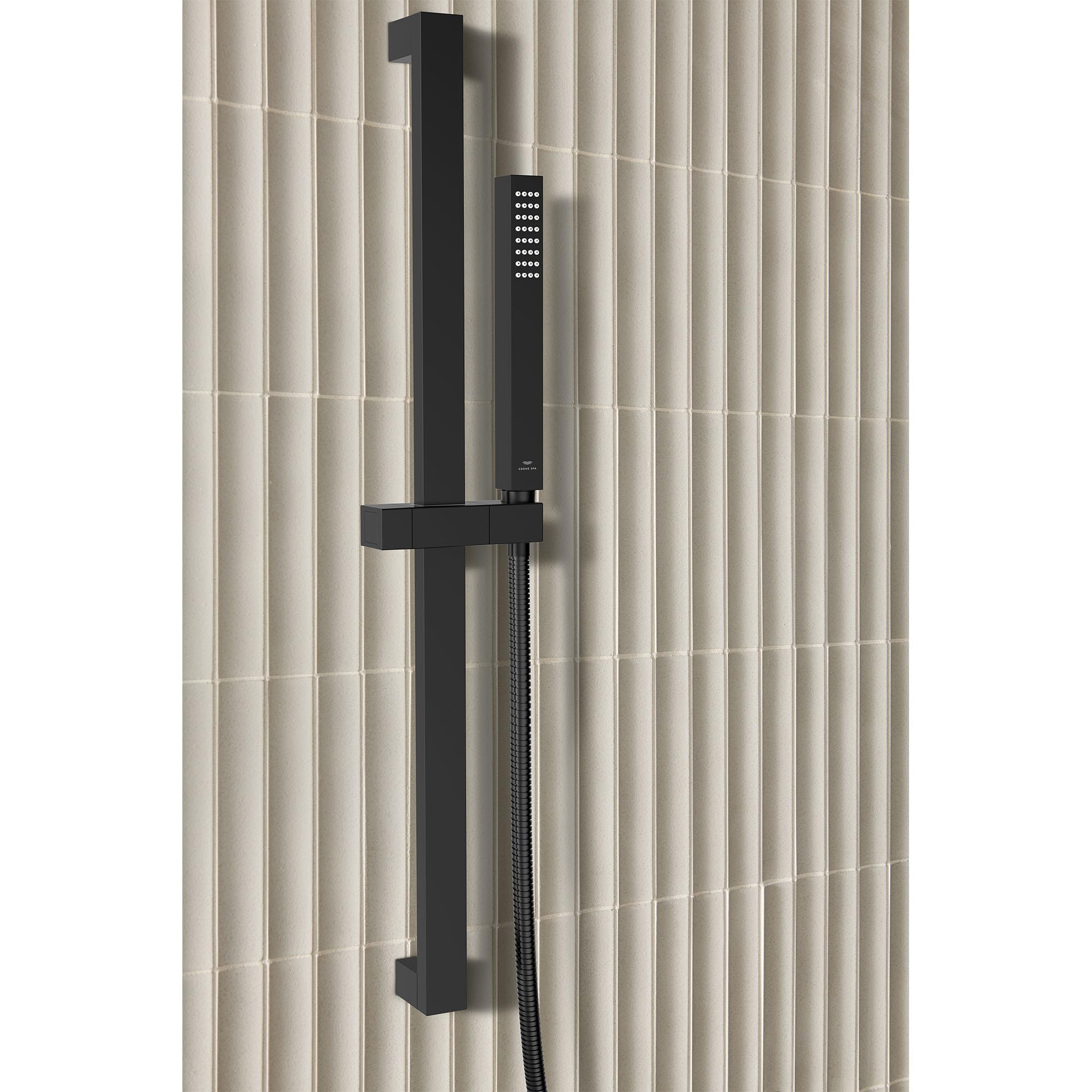 Matte black rectangular hand shower with cube-shaped head mounted on vertical rail with hose against tiled wall.