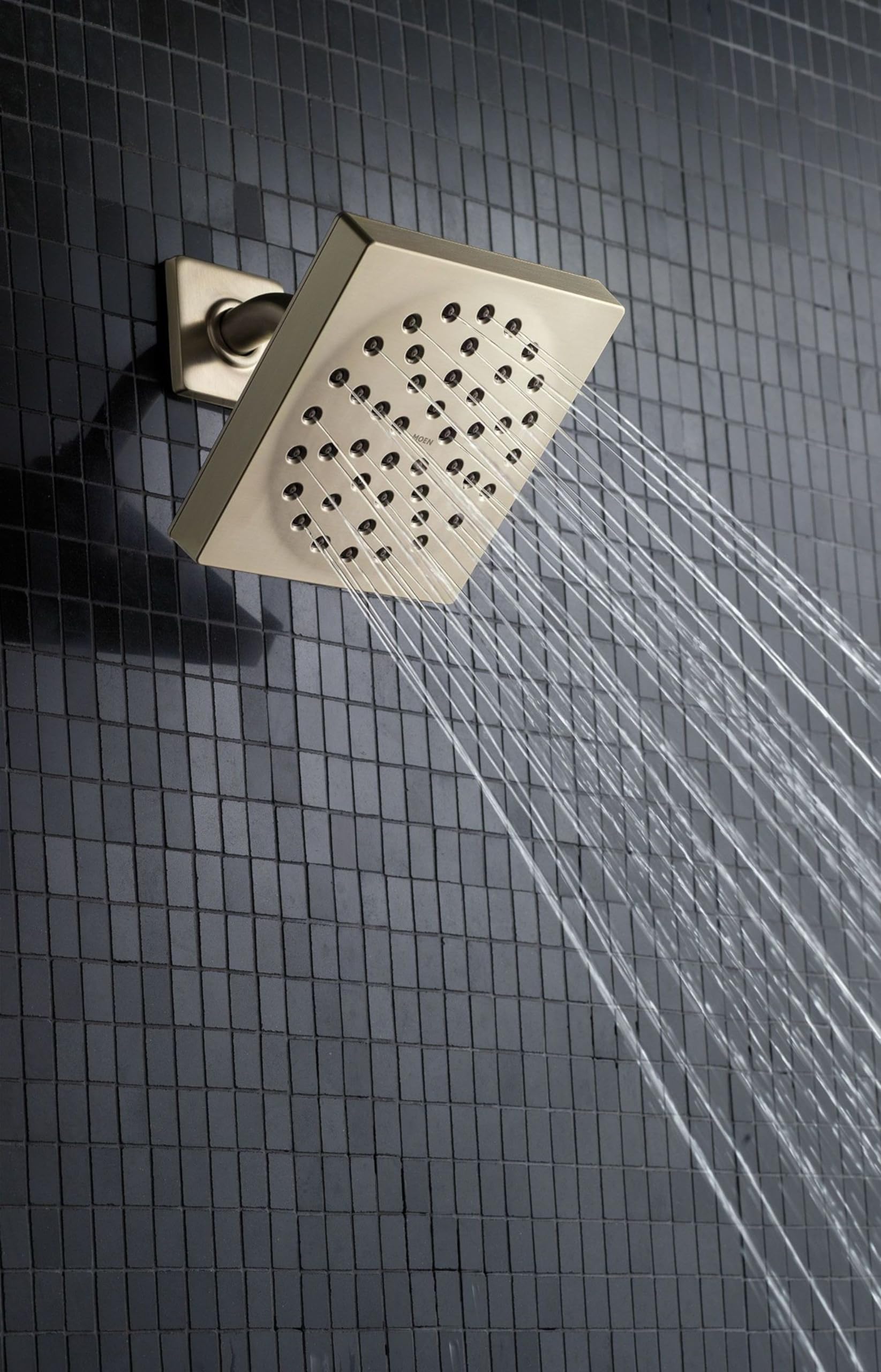 Brushed nickel square showerhead mounted on wall tile with water streams flowing downward.