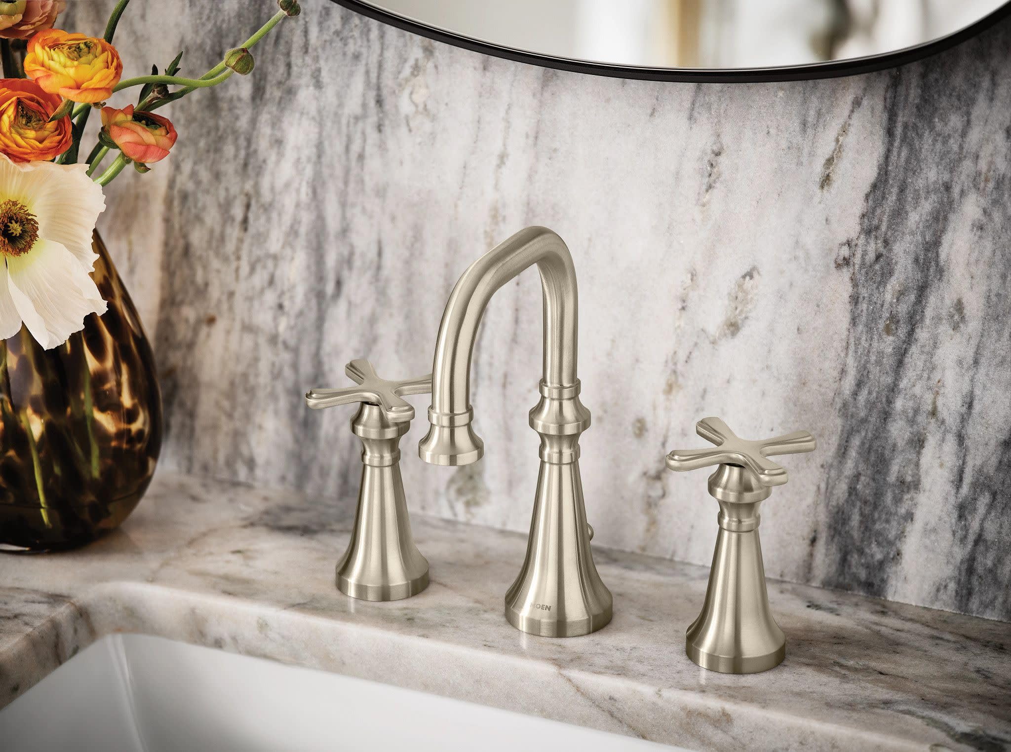 Brushed nickel three-hole bathroom faucet with arched spout and cross handles installed on marble sink counter.