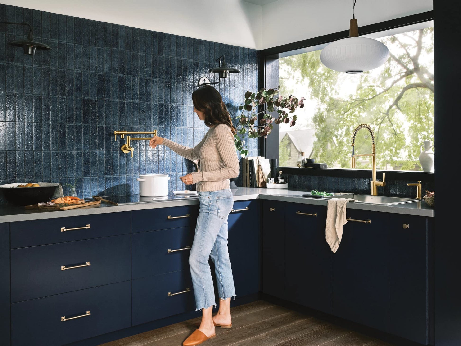 Brushed gold wall-mounted pot filler faucet with double-jointed swing arm extended over stovetop in modern kitchen.