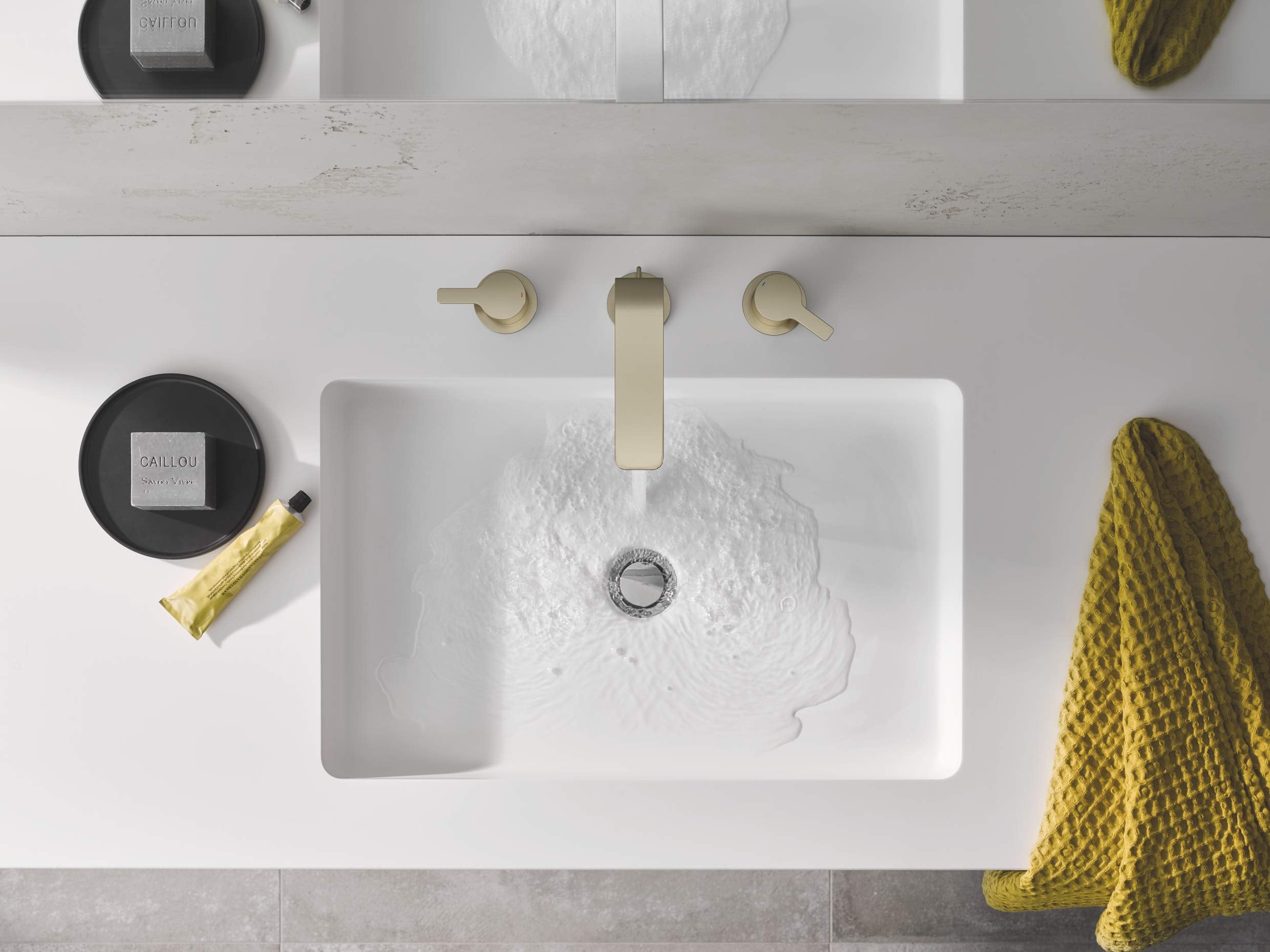 Brushed nickel widespread bathroom faucet with two handles mounted above white rectangular sink with water running.