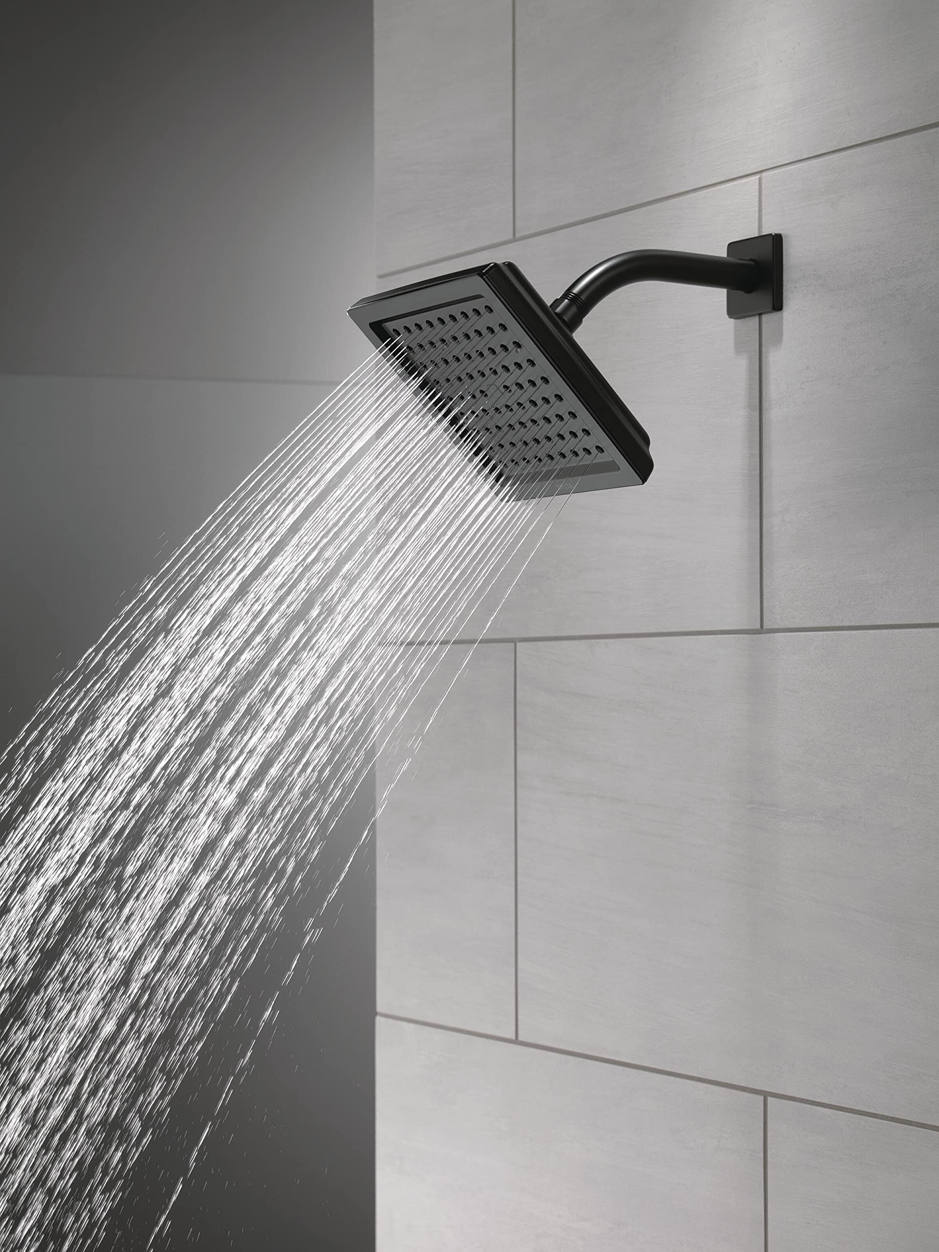 Matte black square raincan shower head mounted on wall with water streaming downward.