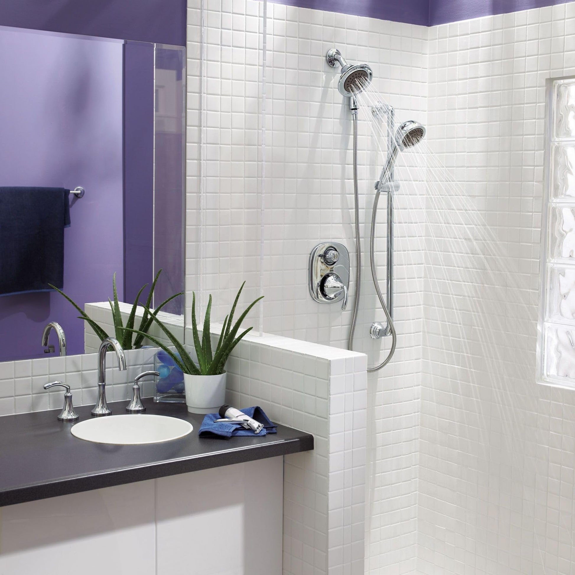 Chrome showerhead with handheld attachment mounted on bathroom wall tile above bathtub enclosure.