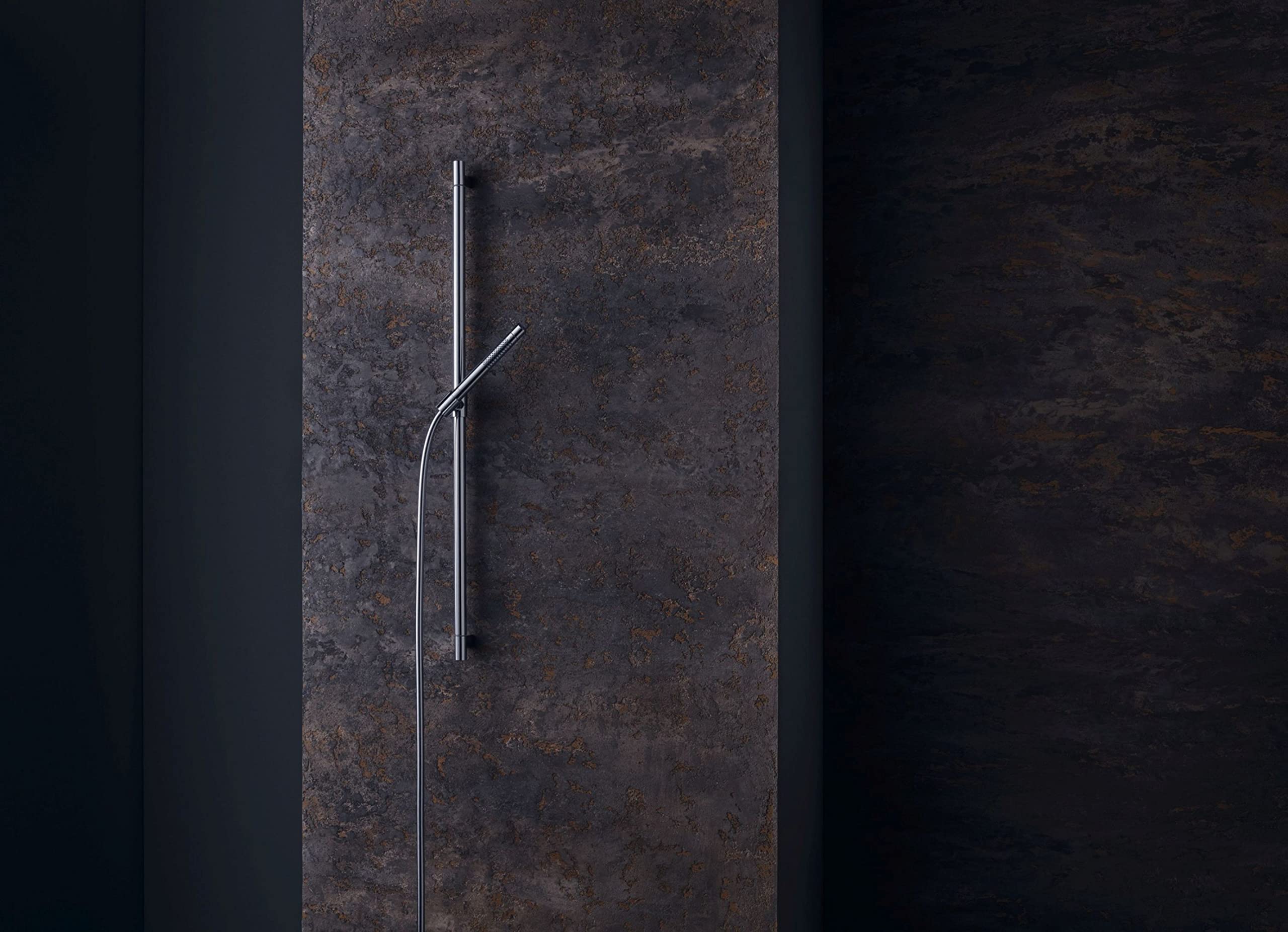 Brushed nickel cylindrical handshower with curved hose against dark textured wall.
