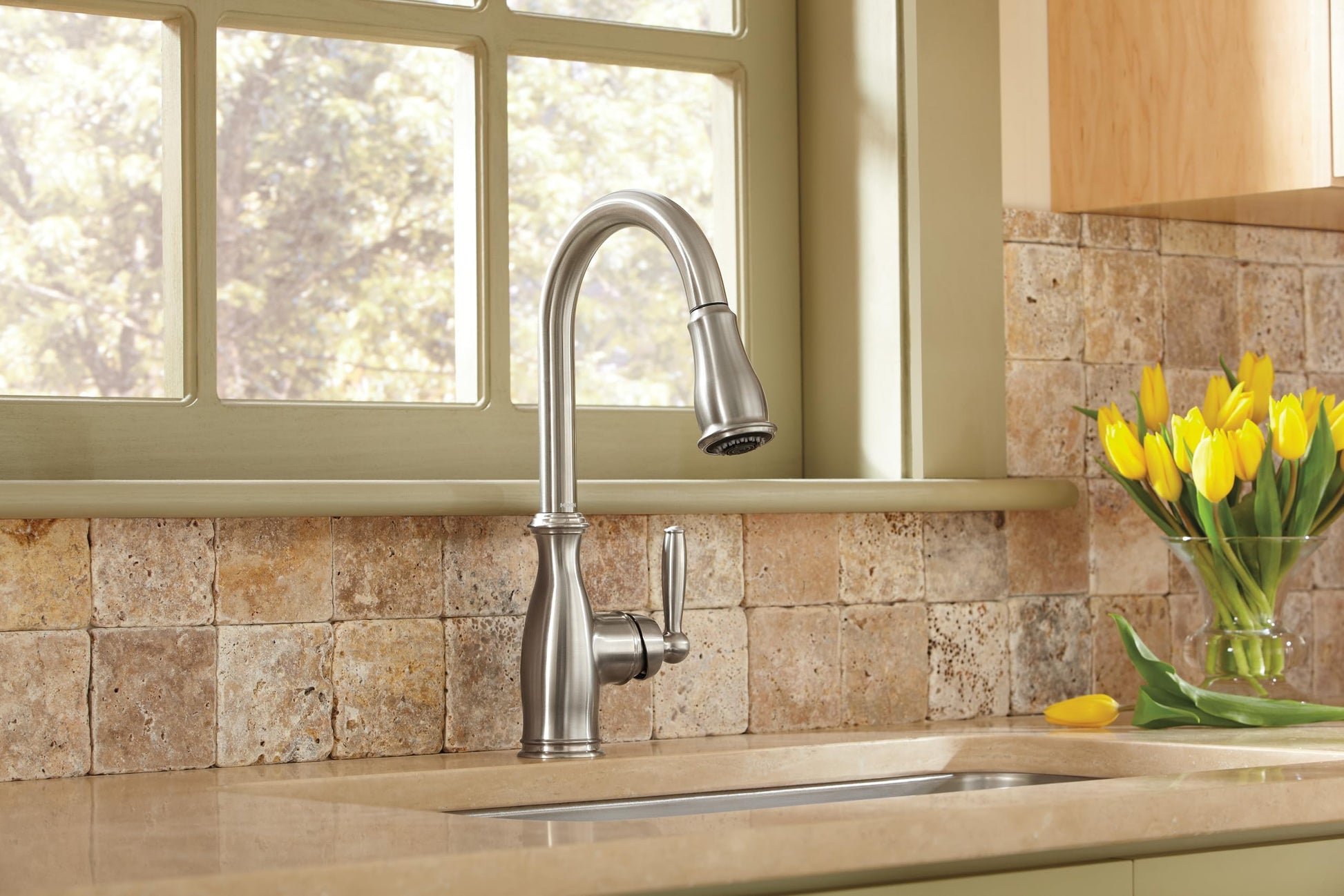Stainless steel pull-down kitchen faucet with side handle installed over sink in beige kitchen with tile backsplash.