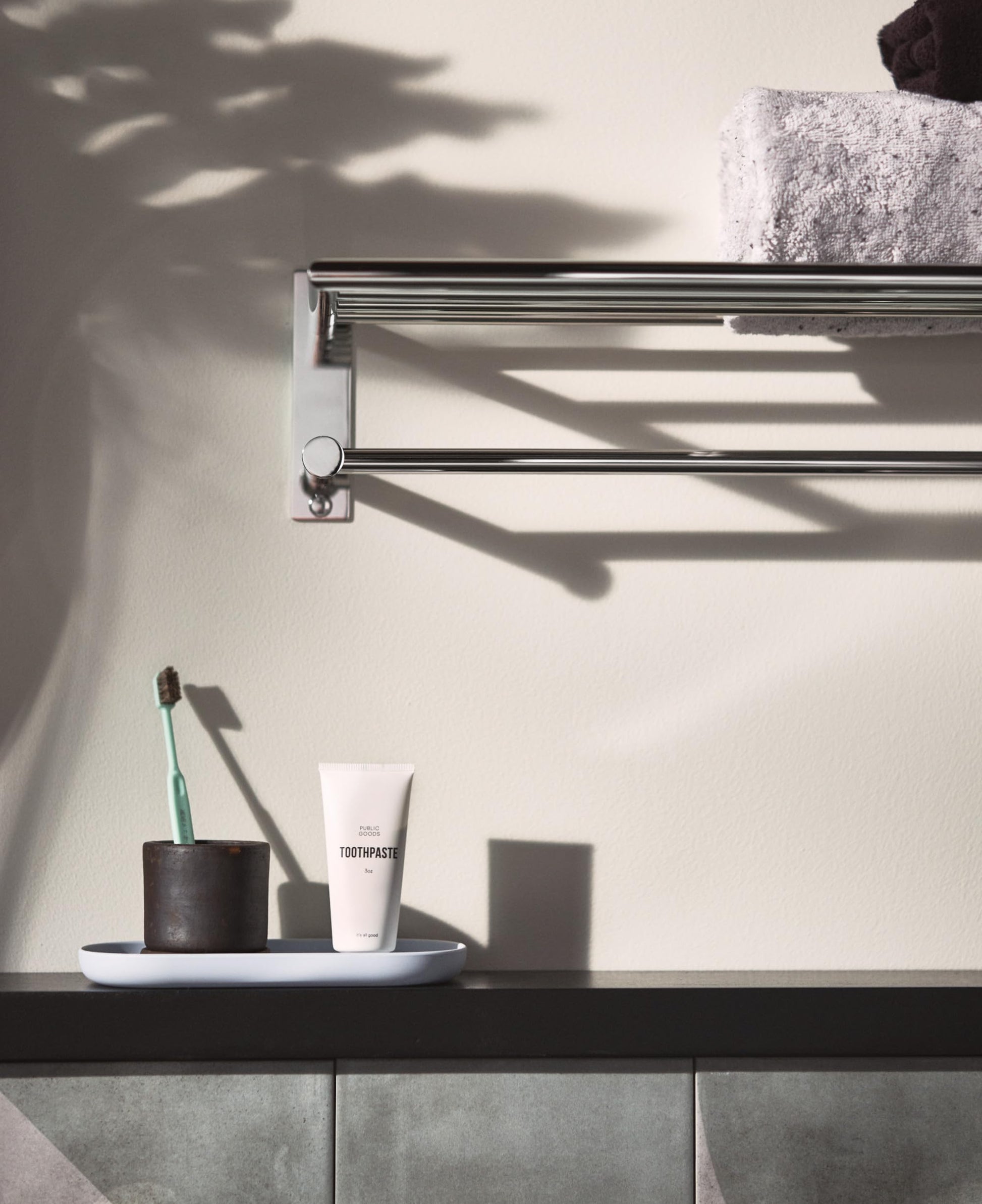 Chrome towel shelf and bar mounted on wall above bathroom counter with folded towel and toiletries displayed.