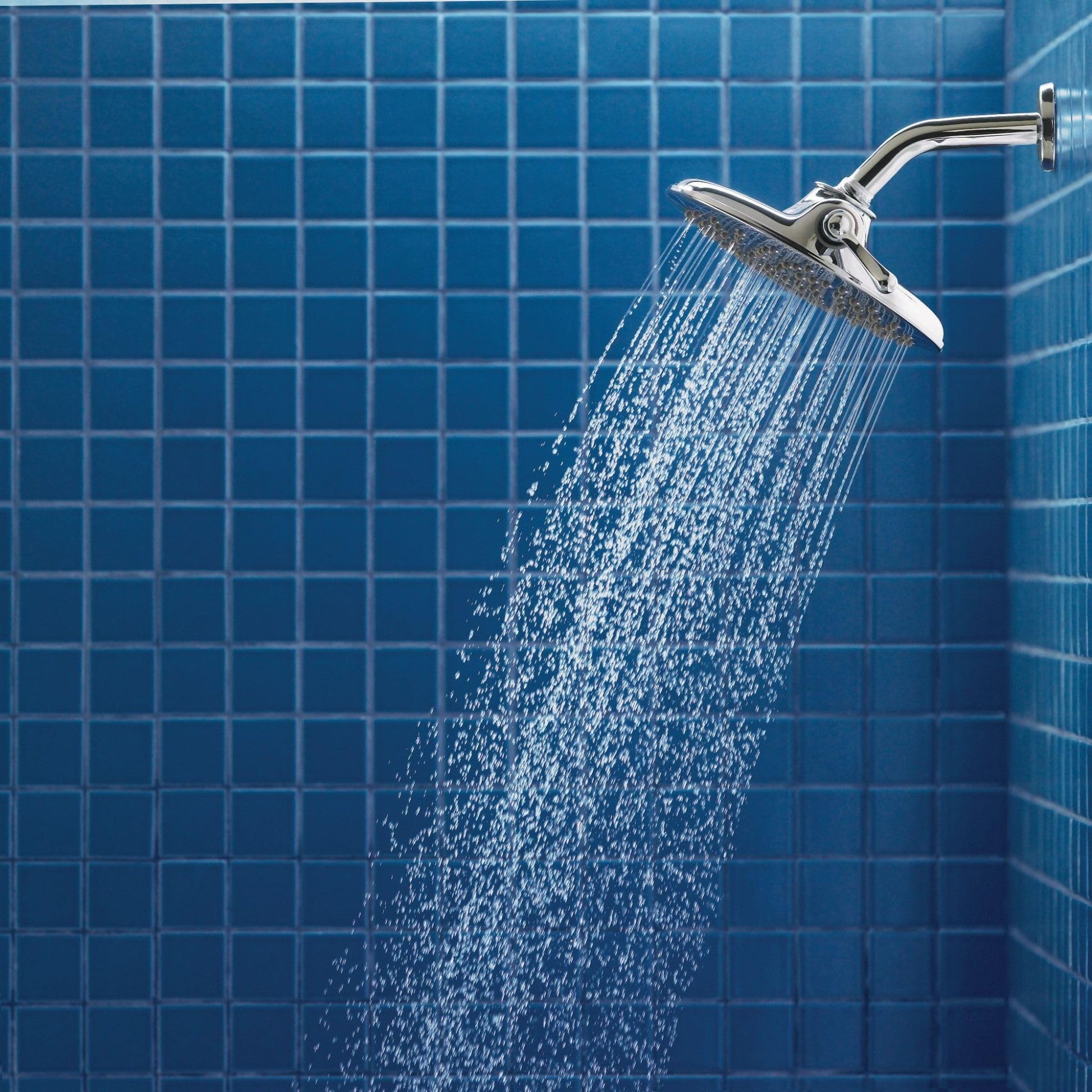 Chrome rainfall showerhead with curved arm mounted on blue tile wall with water flowing downward.