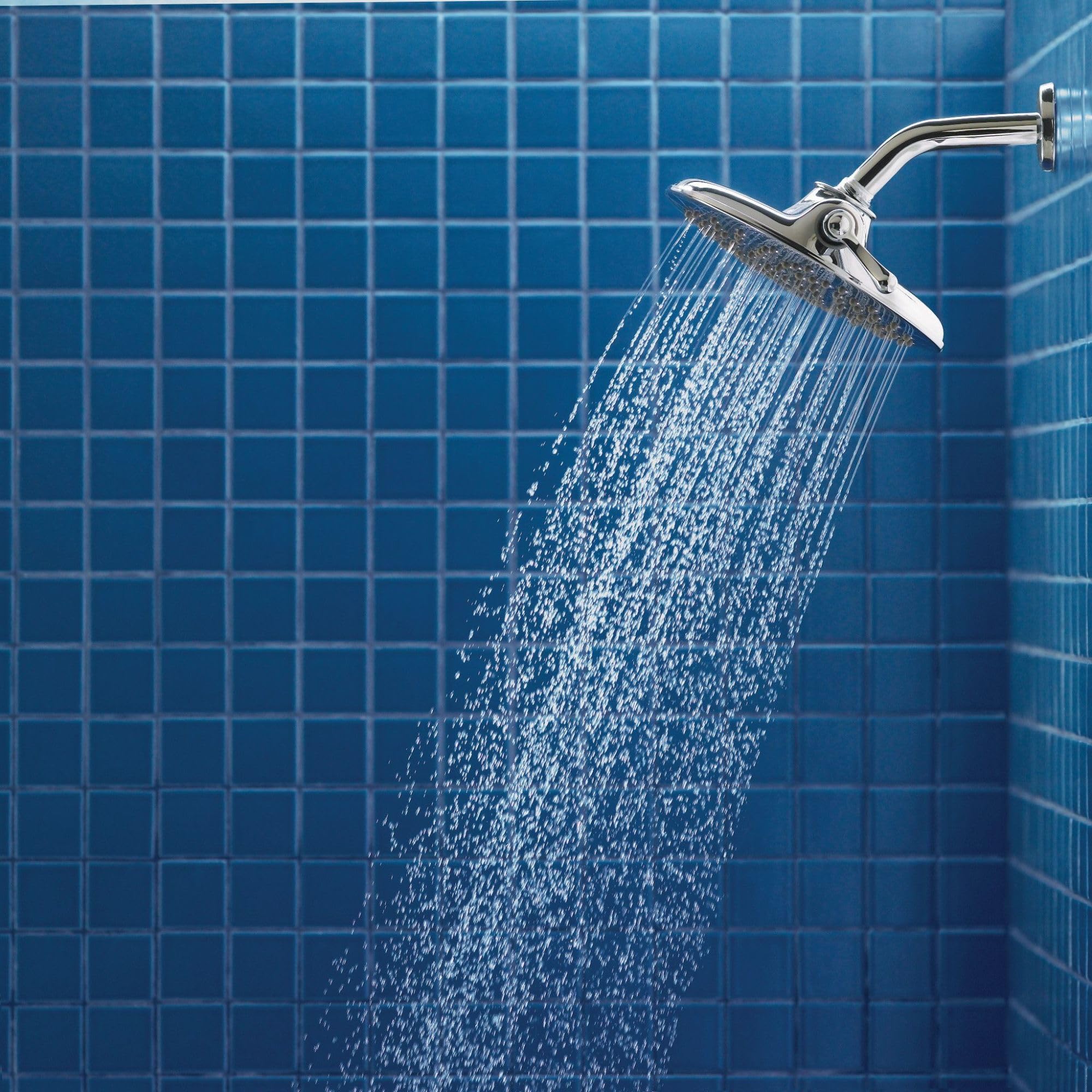 Chrome rainfall showerhead with curved arm mounted on blue tiled bathroom wall, dispensing water.