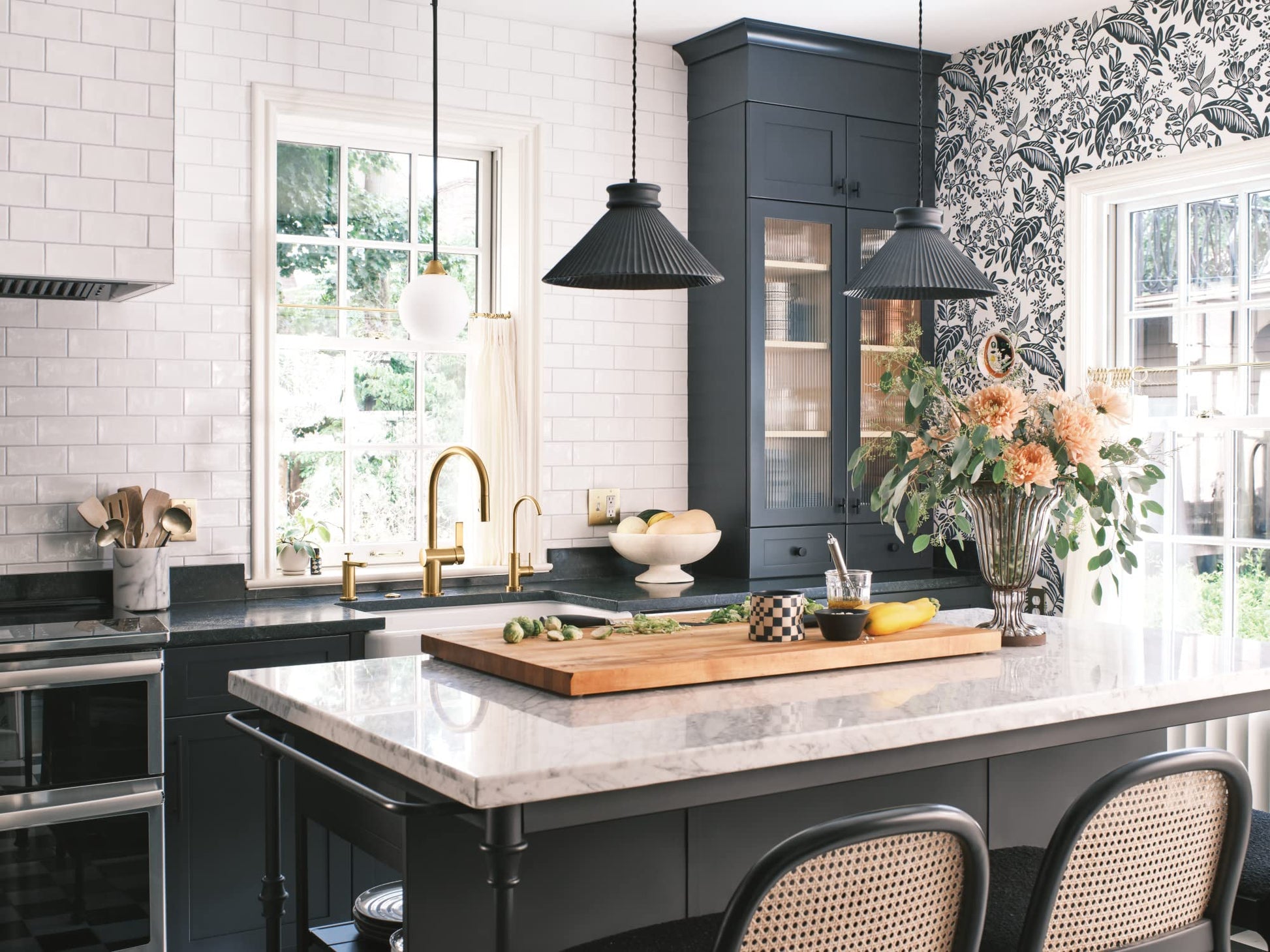 Brushed gold pulldown kitchen faucet with dual handles mounted on black countertop in modern kitchen.