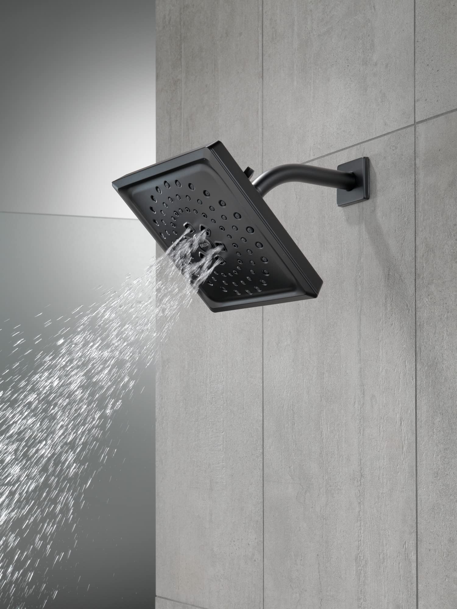 Matte black shower arm with curved design mounted to tile wall, connected to square showerhead with perforations dispensing w