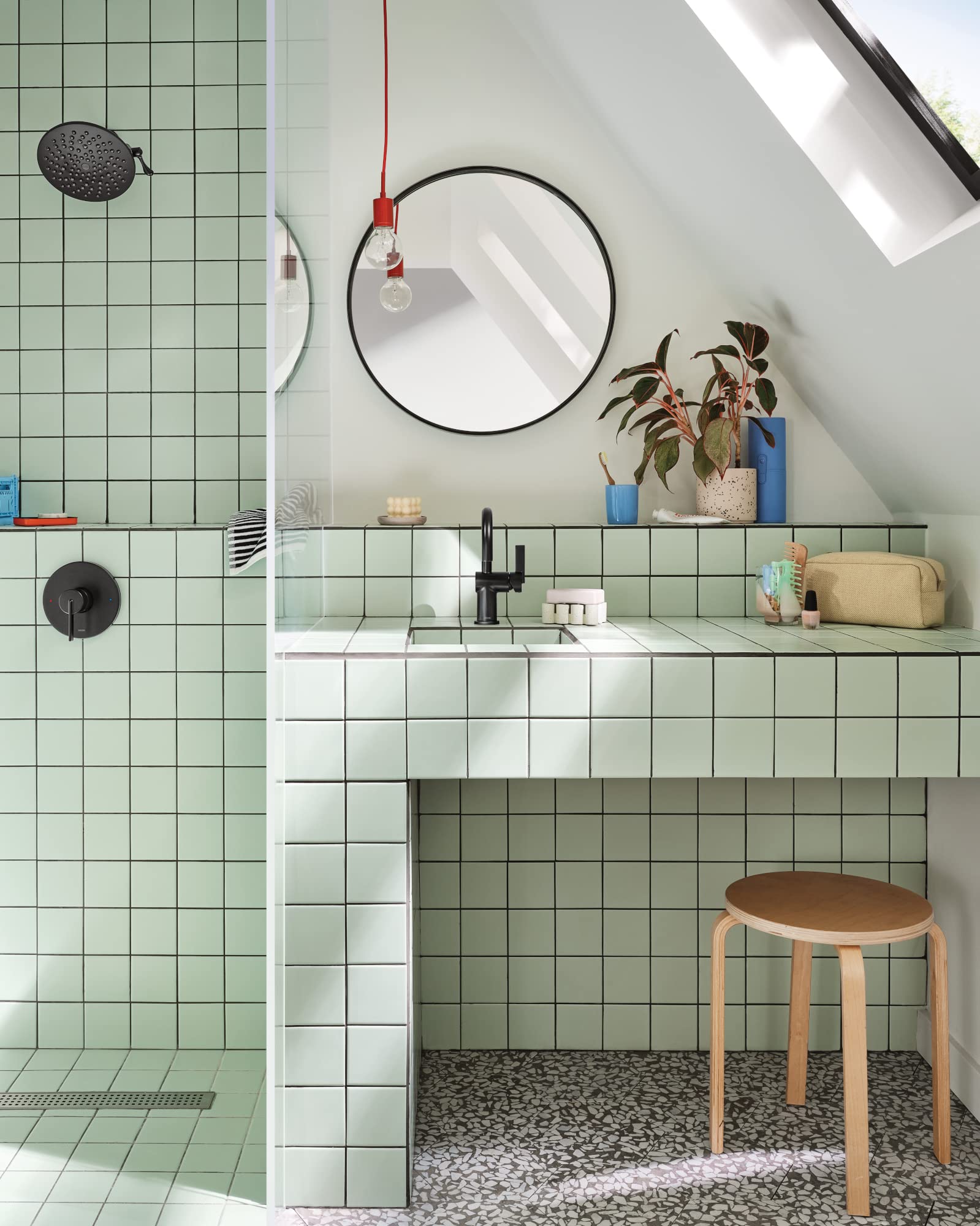 Matte black 8-inch round rainshower spray head mounted on bathroom wall above green tile.