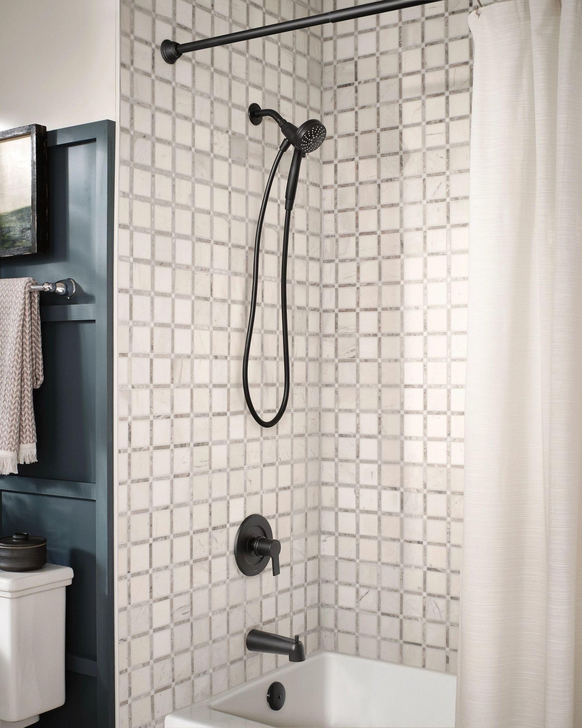 Matte black hand shower with curved hose and perforated shower head mounted in bathroom shower enclosure.