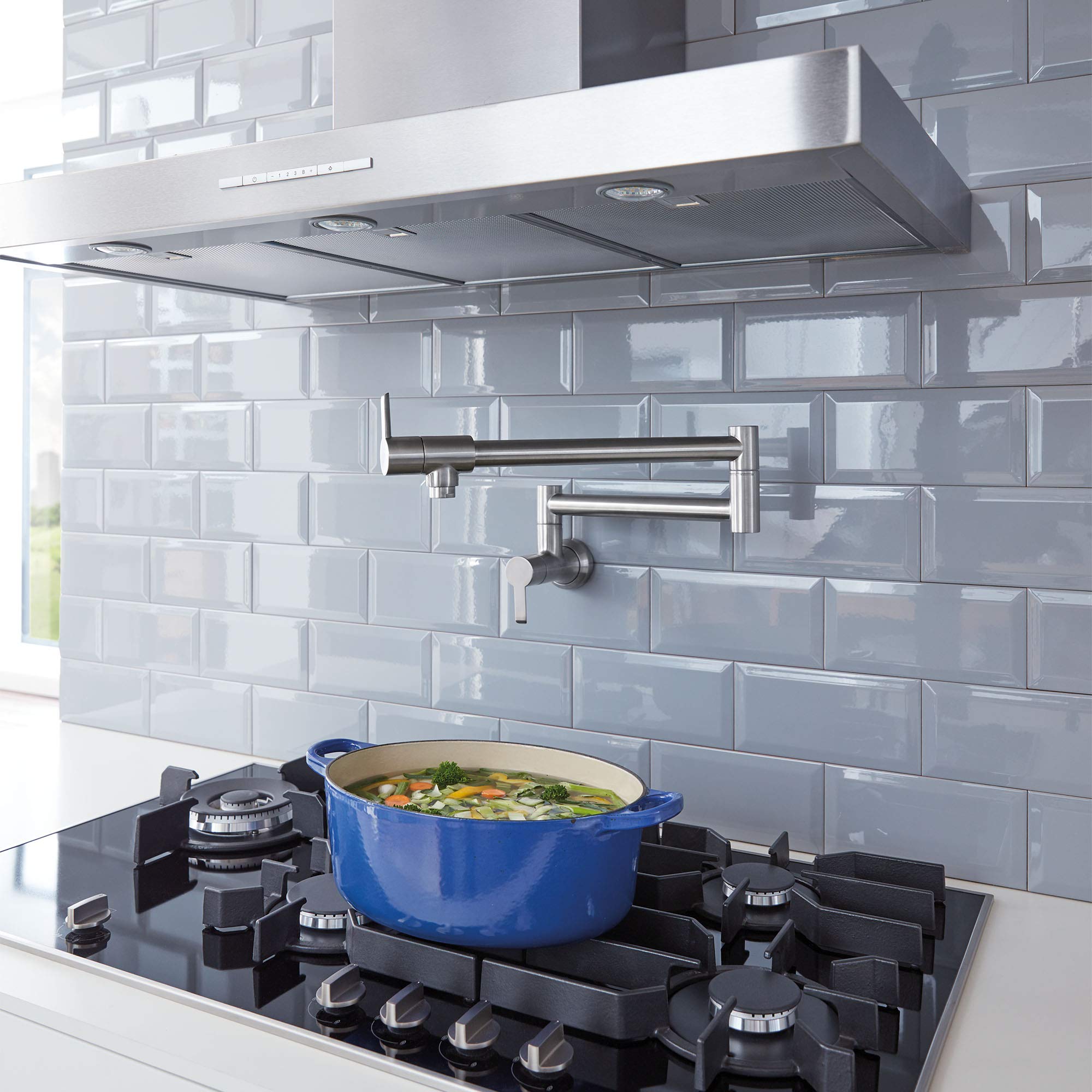 Stainless steel wall-mounted pot filler faucet with two handles installed above a gas cooktop with a blue pot.