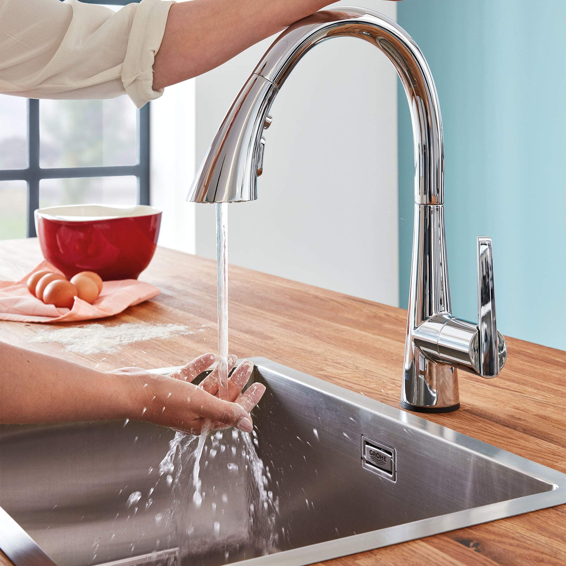 Chrome pull-down kitchen faucet with curved spout dispensing water into stainless steel sink.