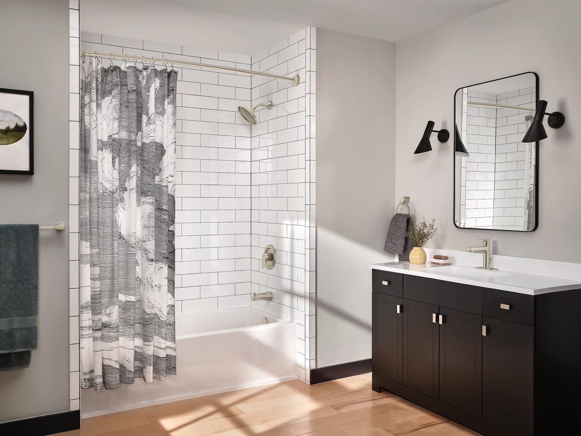 Brushed nickel curved shower curtain rod installed above bathtub with gray patterned shower curtain.