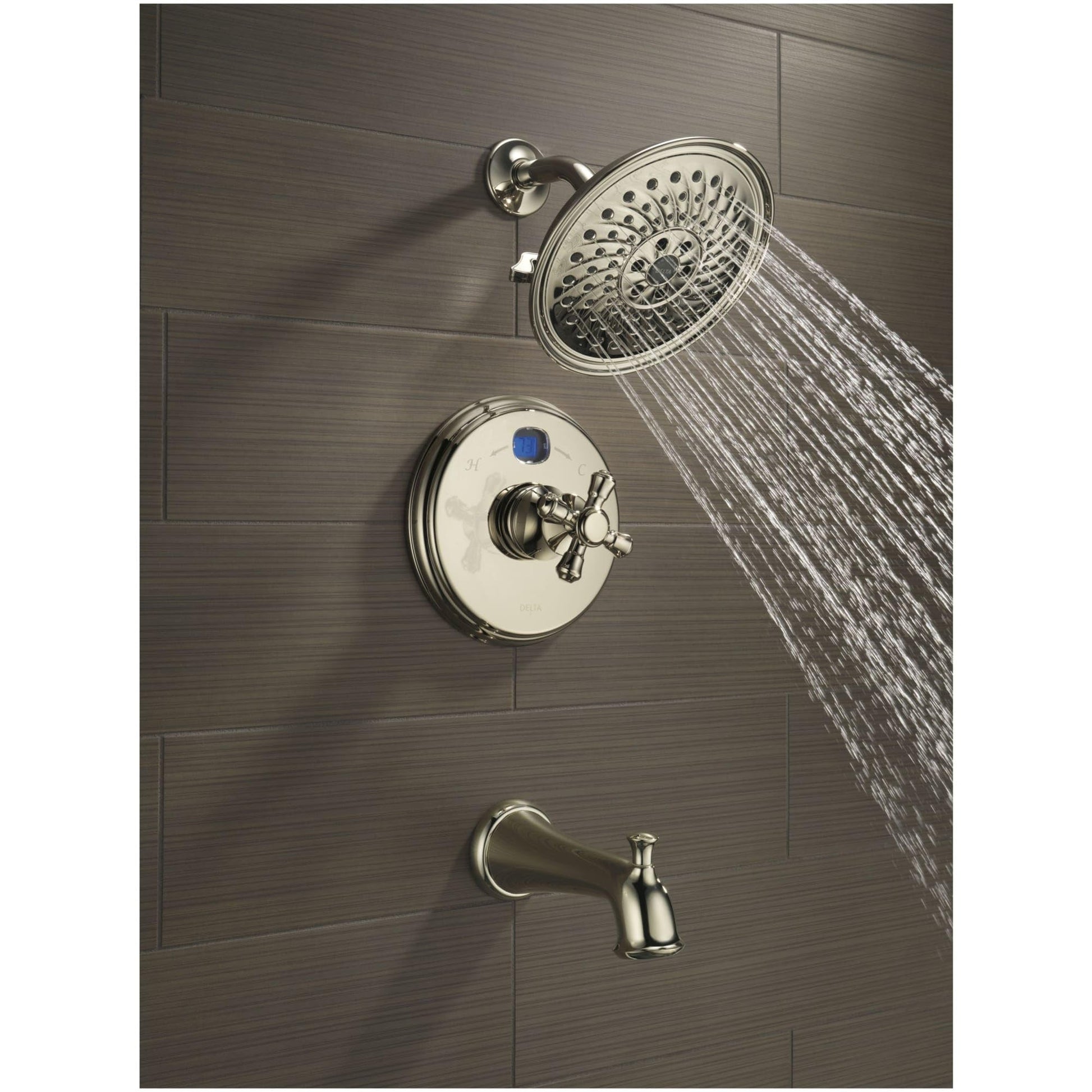 Polished nickel shower system with round showerhead, control valve with cross handles, and tub spout mounted on gray tile wal