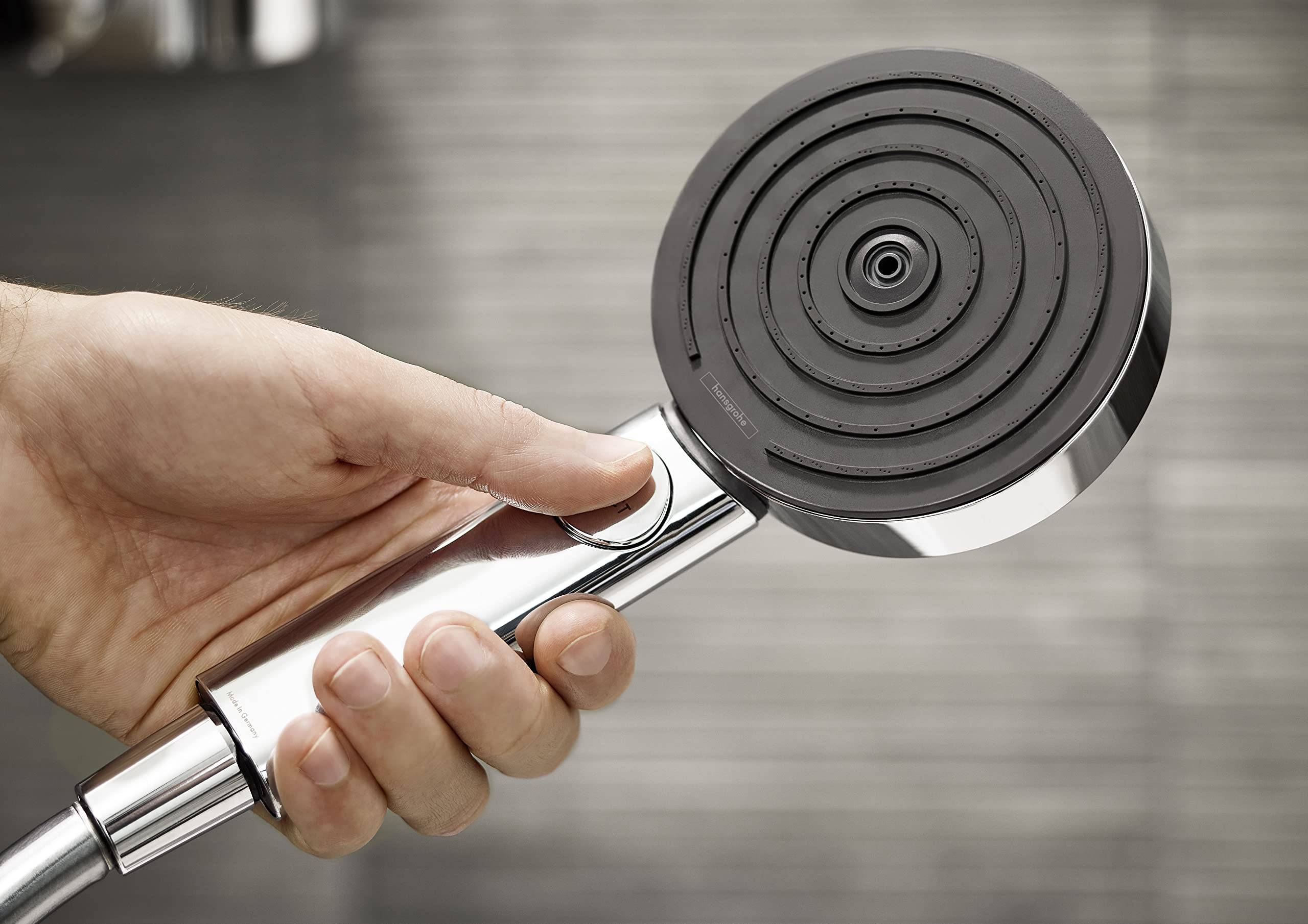 Chrome handheld showerhead with circular jet pattern held in hand, showing concentric spray holes.