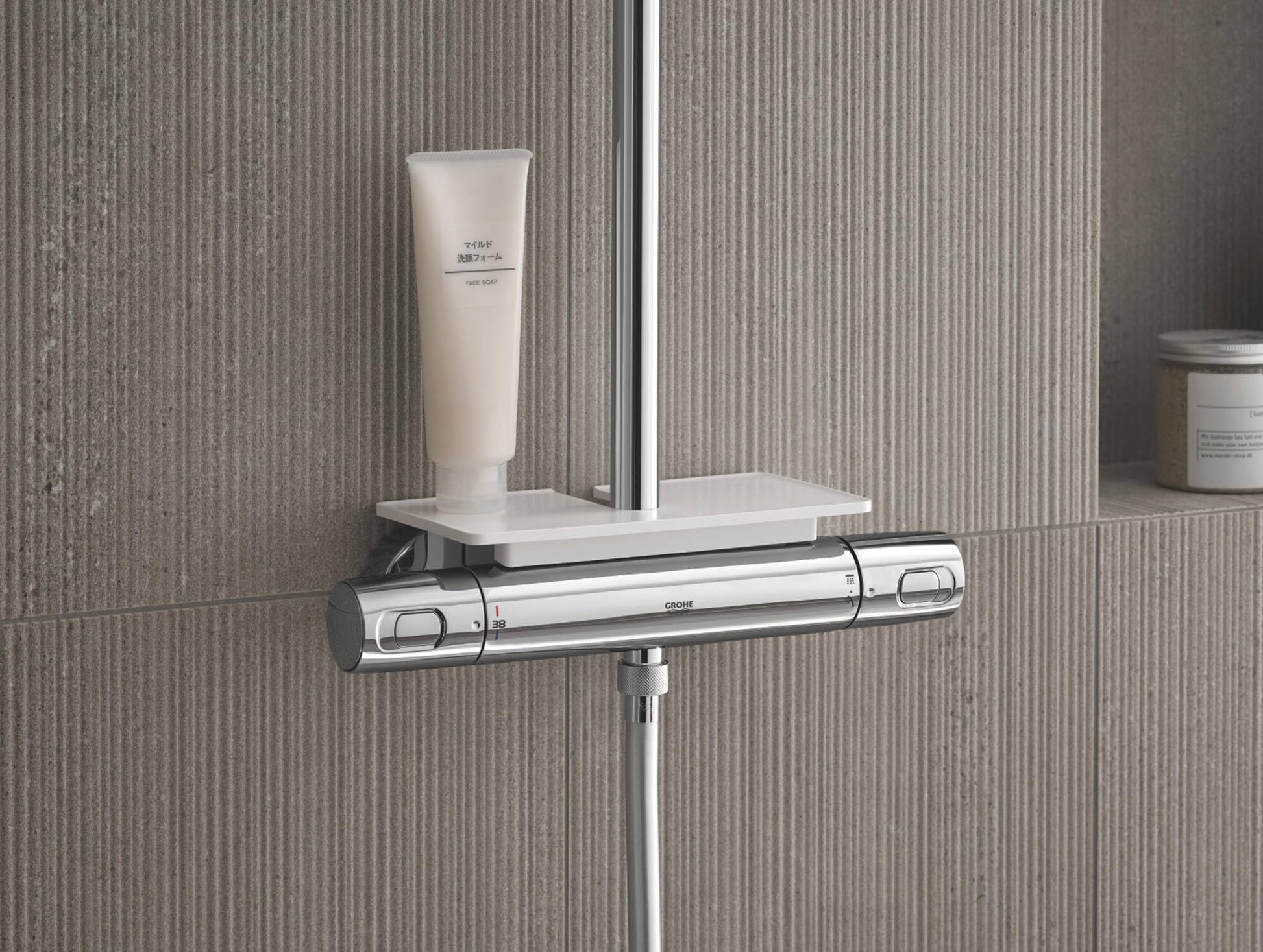 White rectangular shelf mounted above chrome thermostatic valve on shower rail, holding toiletry bottle.