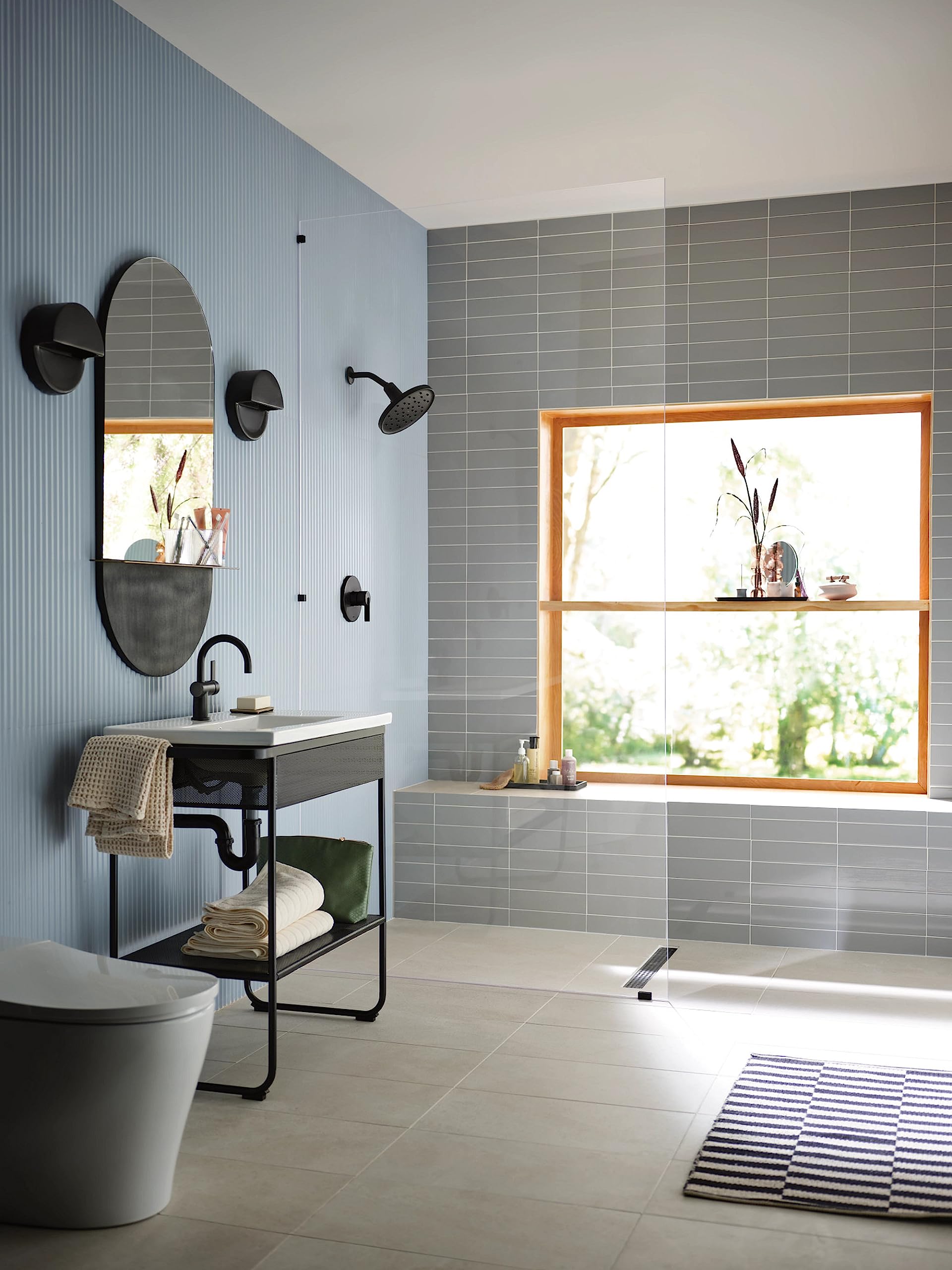 Matte black circular rainshower spray head mounted on bathroom wall above bathtub with gray tile surround.