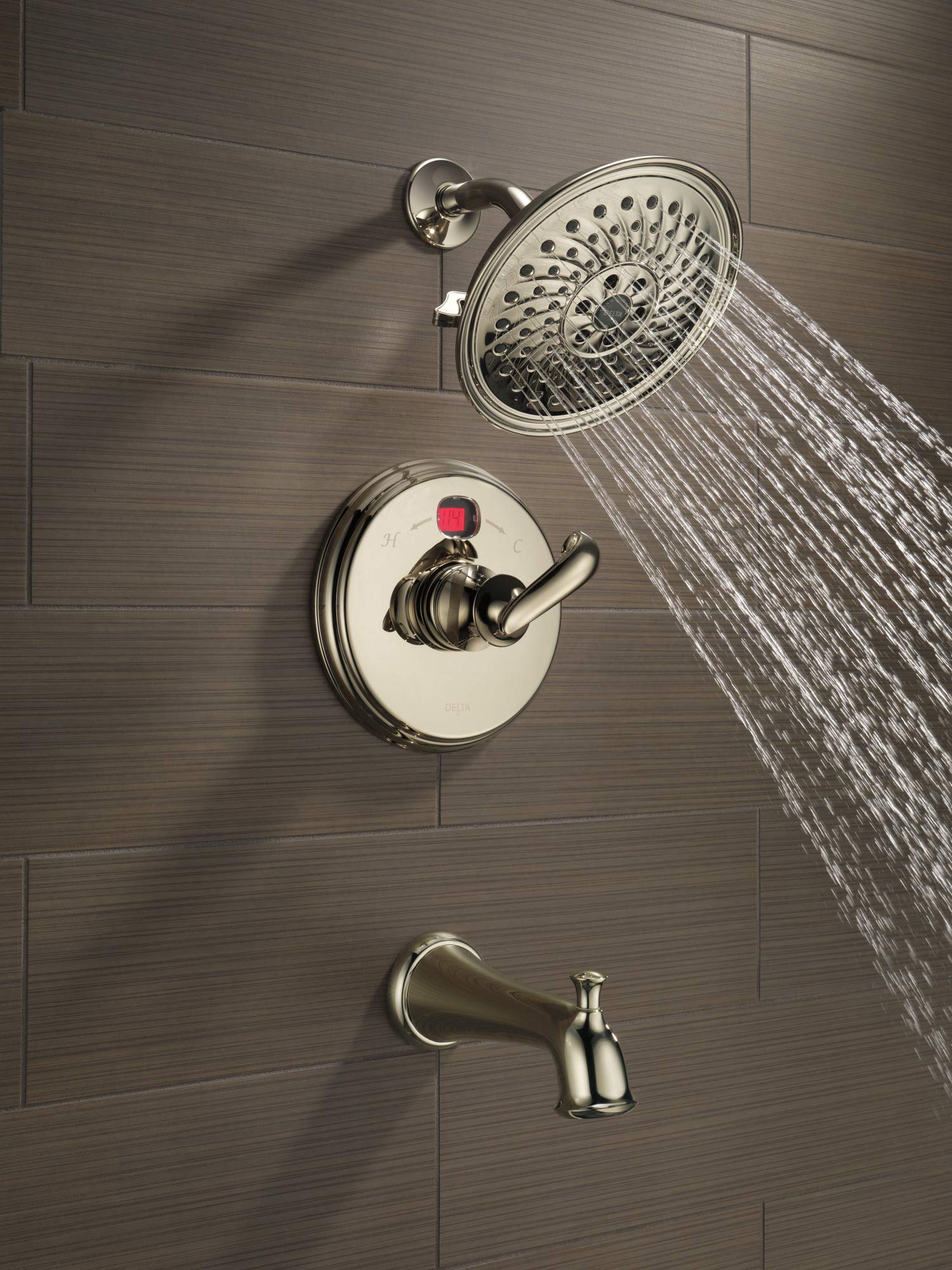 Polished nickel shower system mounted on tile wall with round showerhead, control valve with red indicator, and tub spout.