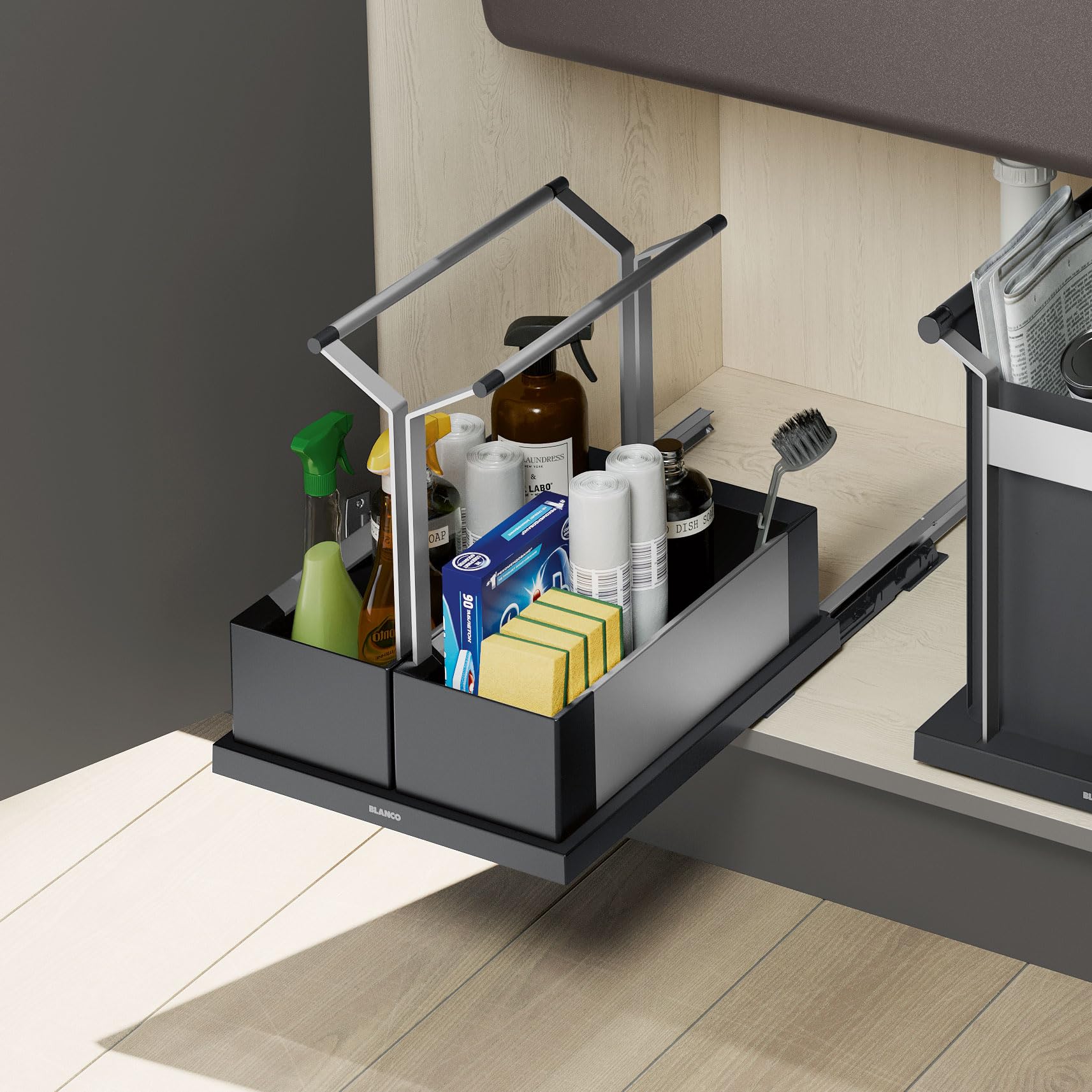 Black double storage caddy with two compartments holding cleaning supplies, paper towels, and kitchen items on a sink counter