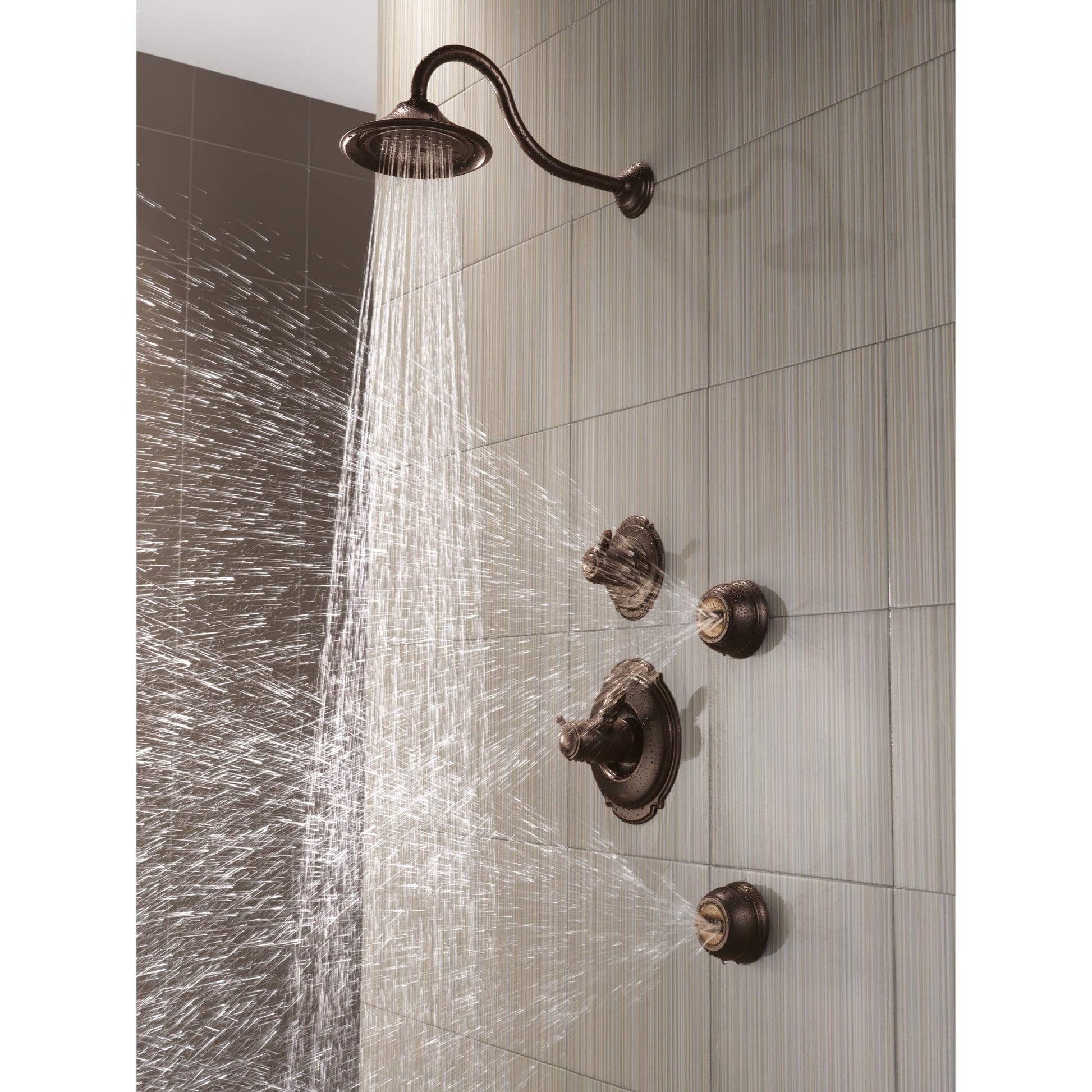 Venetian bronze shower head with curved arm mounted on tiled bathroom wall, dispensing water spray.