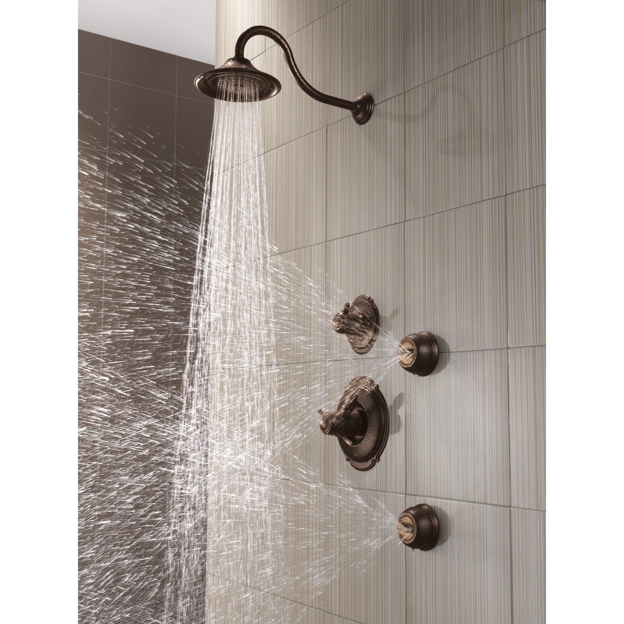 Venetian bronze shower head with curved arm mounted on tiled bathroom wall, dispensing water spray.