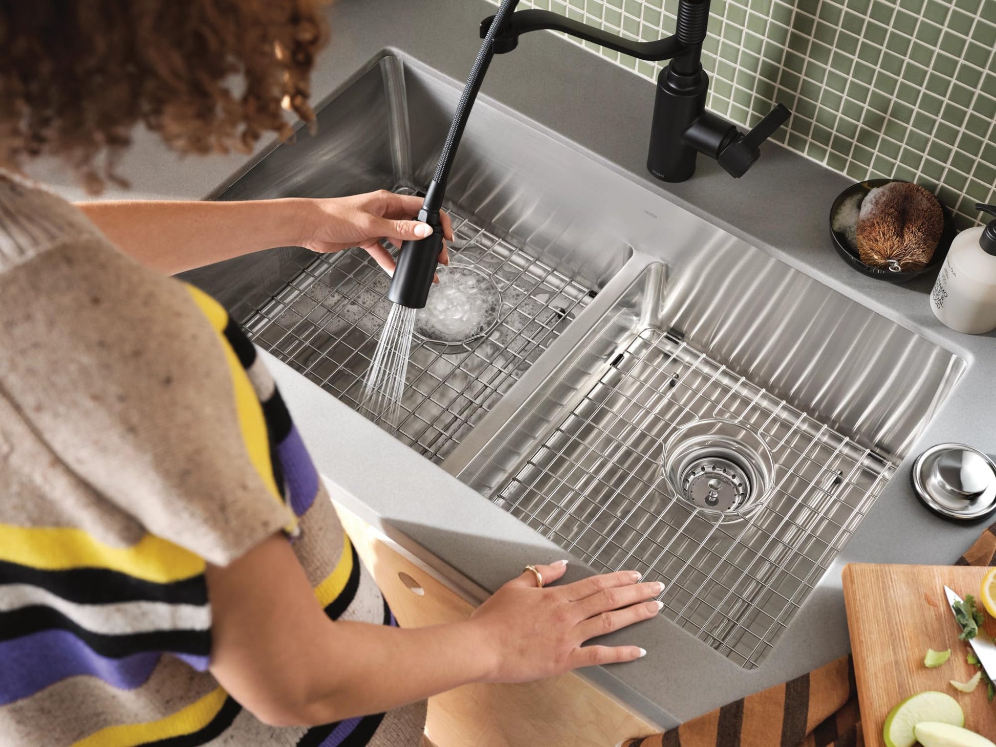 Stainless steel double bowl kitchen sink with low divide, bottom grids, and black pull-down faucet installed in countertop.