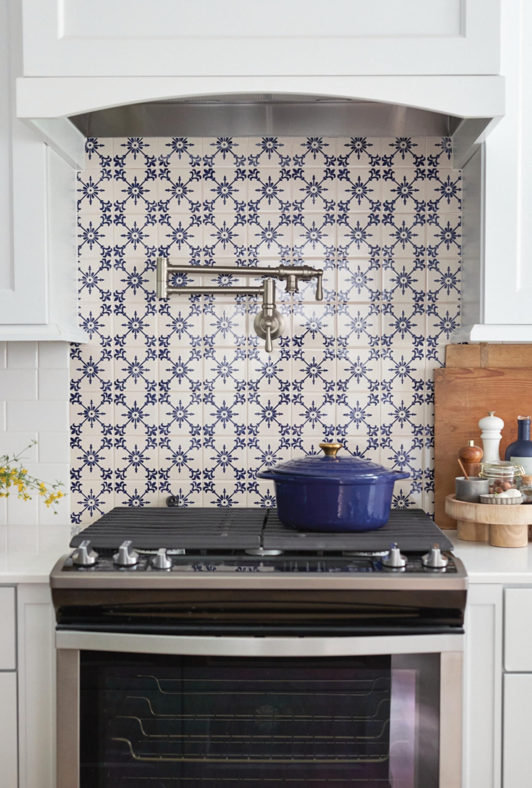 Stainless steel wall-mount pot filler faucet with folding swing arm mounted above kitchen stovetop.