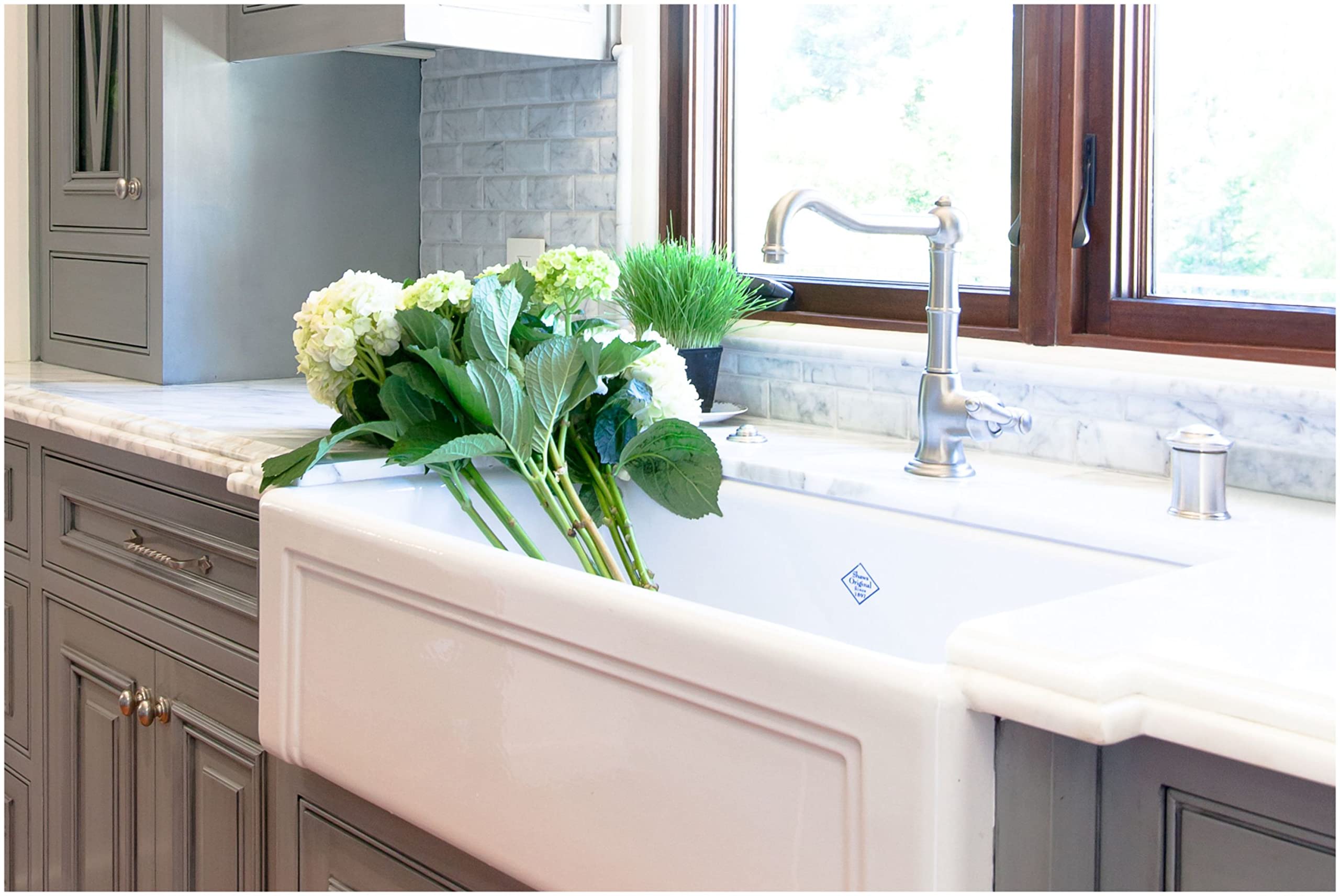 White fireclay farmhouse apron front sink with single bowl, installed in kitchen countertop with faucet and decorative flower