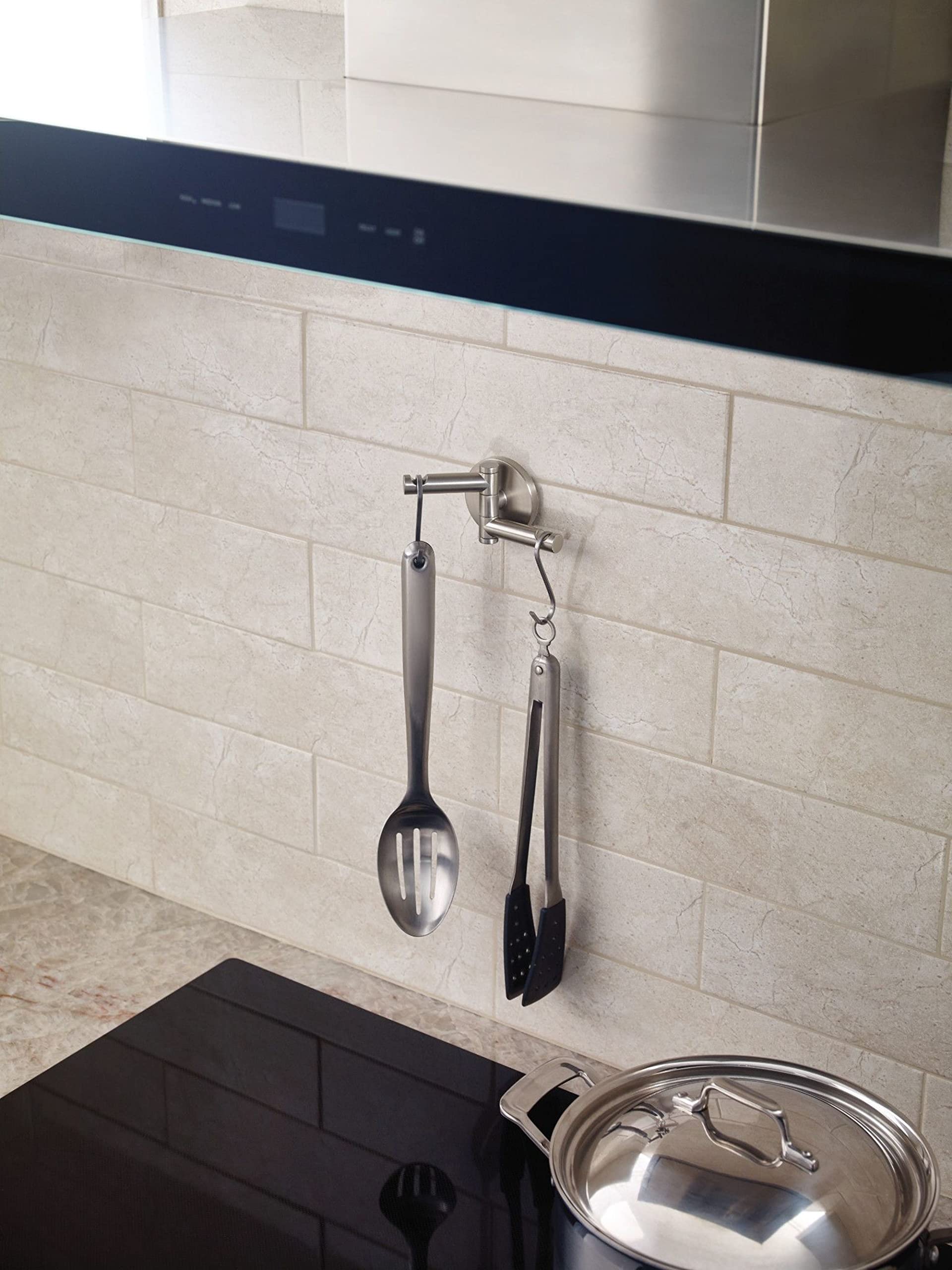 Brushed nickel swivel double robe hook mounted on subway tile backsplash with kitchen utensils hanging from it.