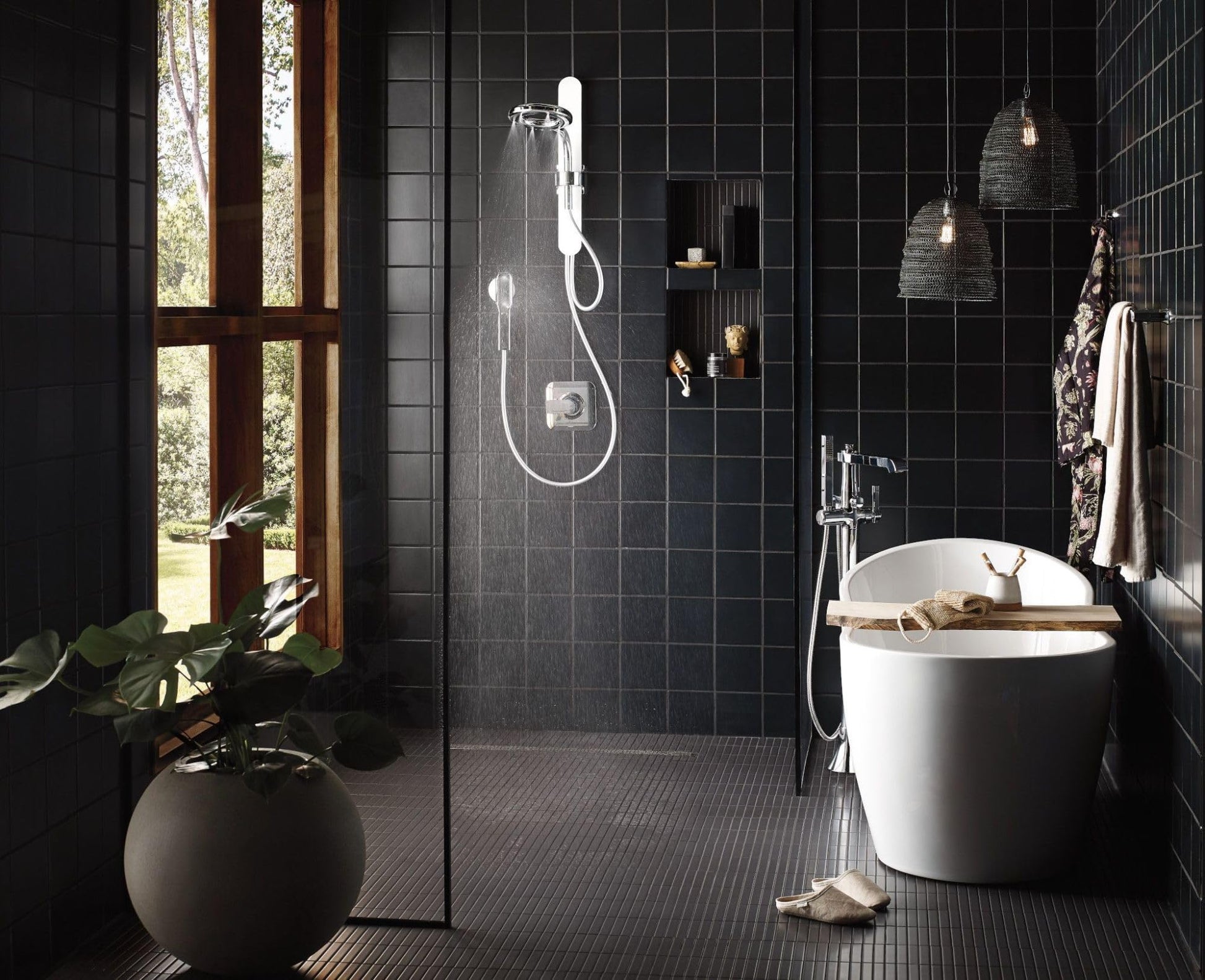 Chrome freestanding tub filler with single handle and detachable handshower mounted next to white soaking tub.