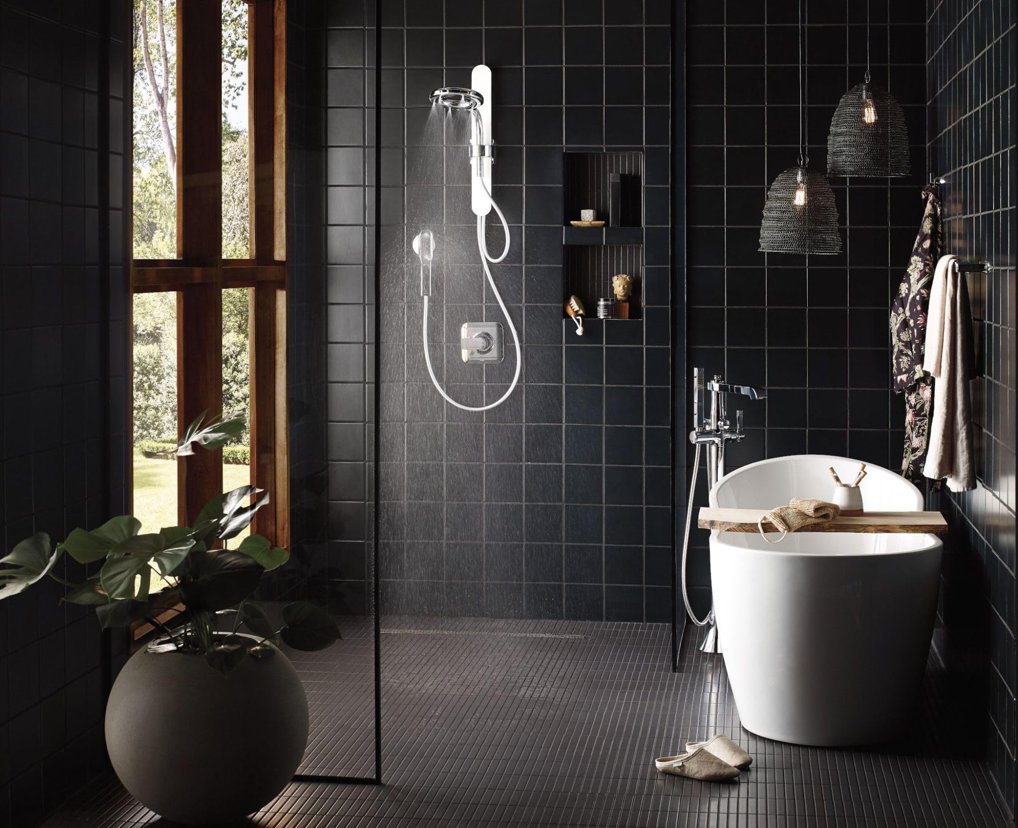 Chrome freestanding tub filler with single handle and detachable handshower mounted next to white soaking tub.