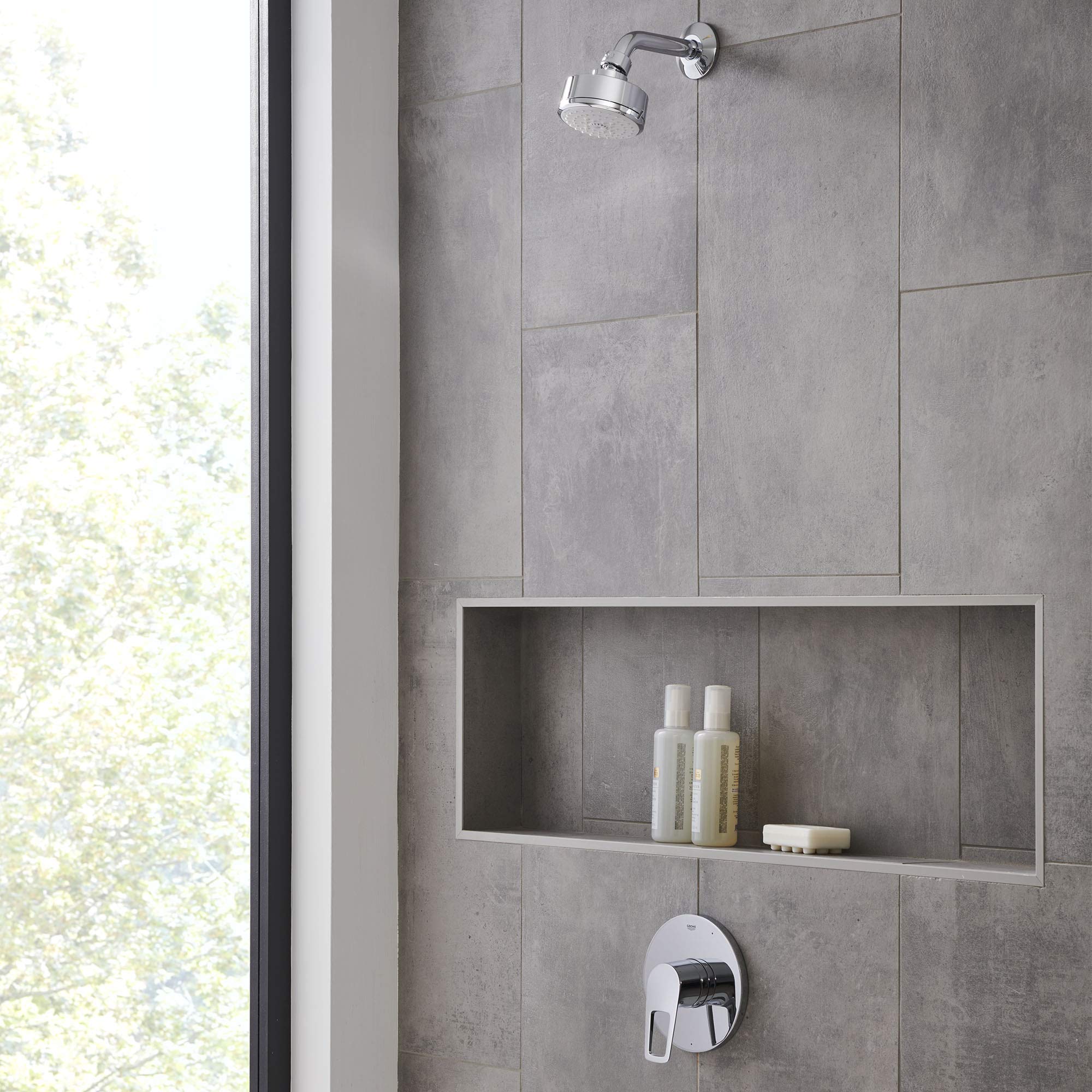 Chrome pressure balance valve trim with single handle control mounted on gray tile shower wall below showerhead.