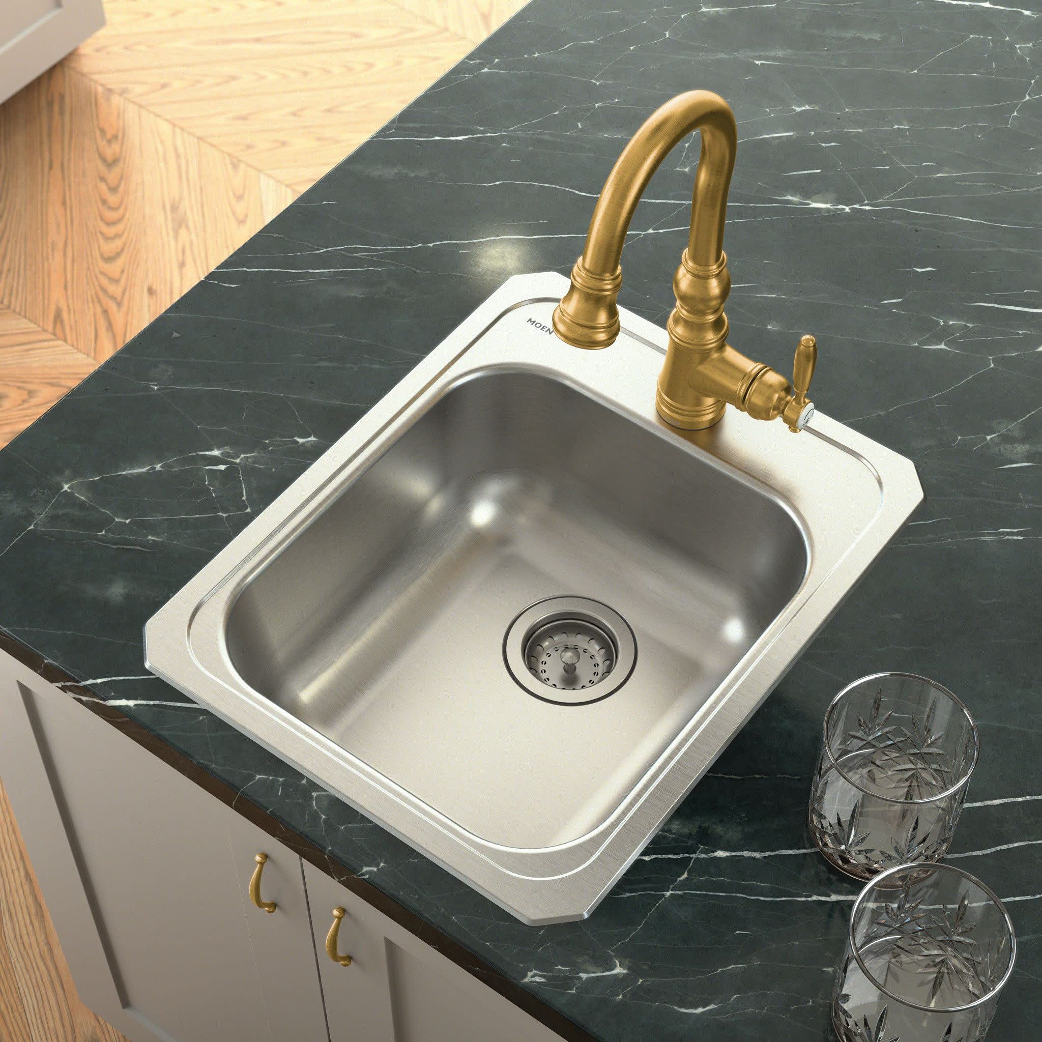 Brushed gold pulldown kitchen faucet with curved spout installed on white sink with black marble countertop.
