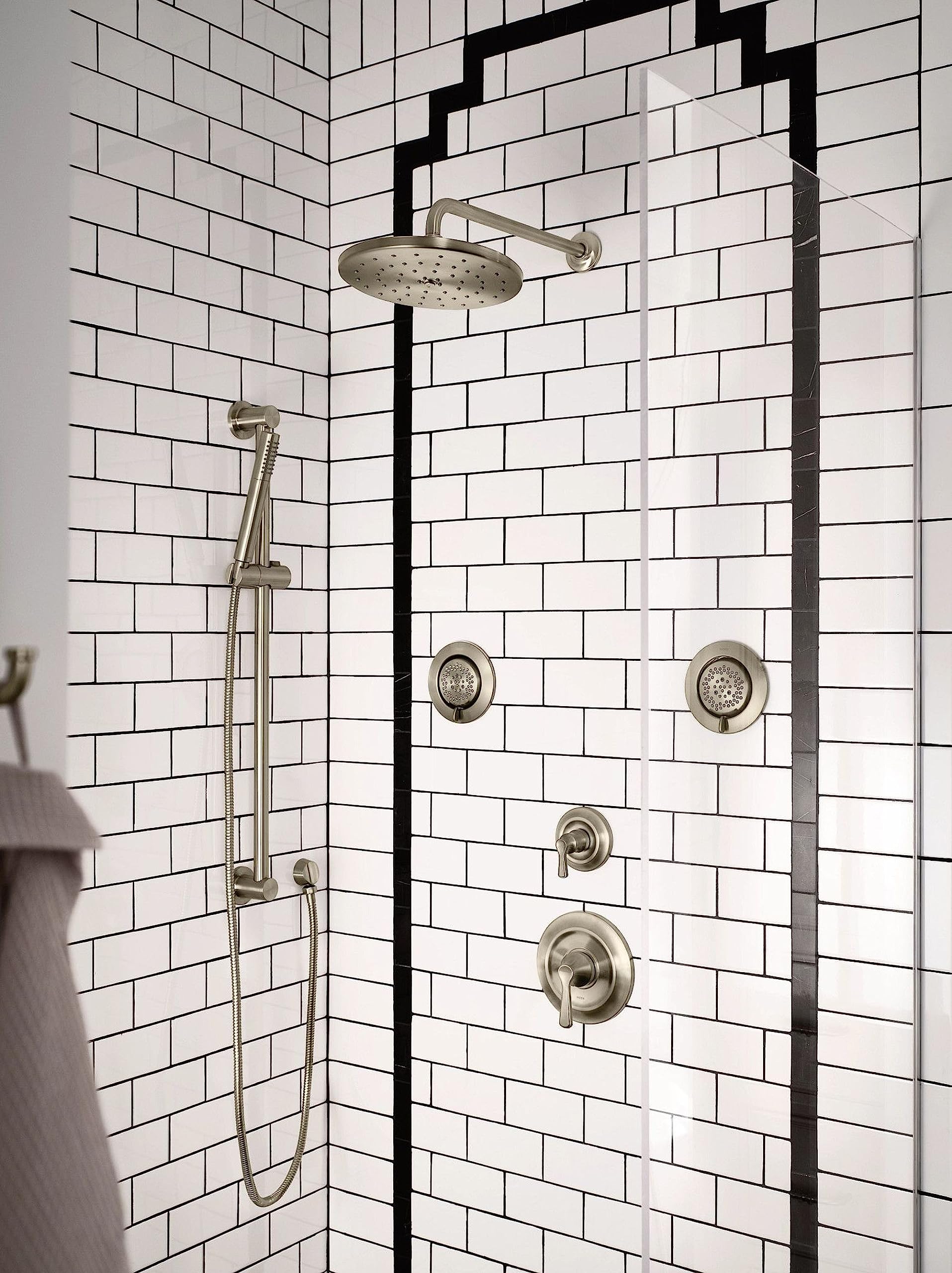 Brushed nickel shower arm flange mounted to white subway tile wall, connecting overhead showerhead.