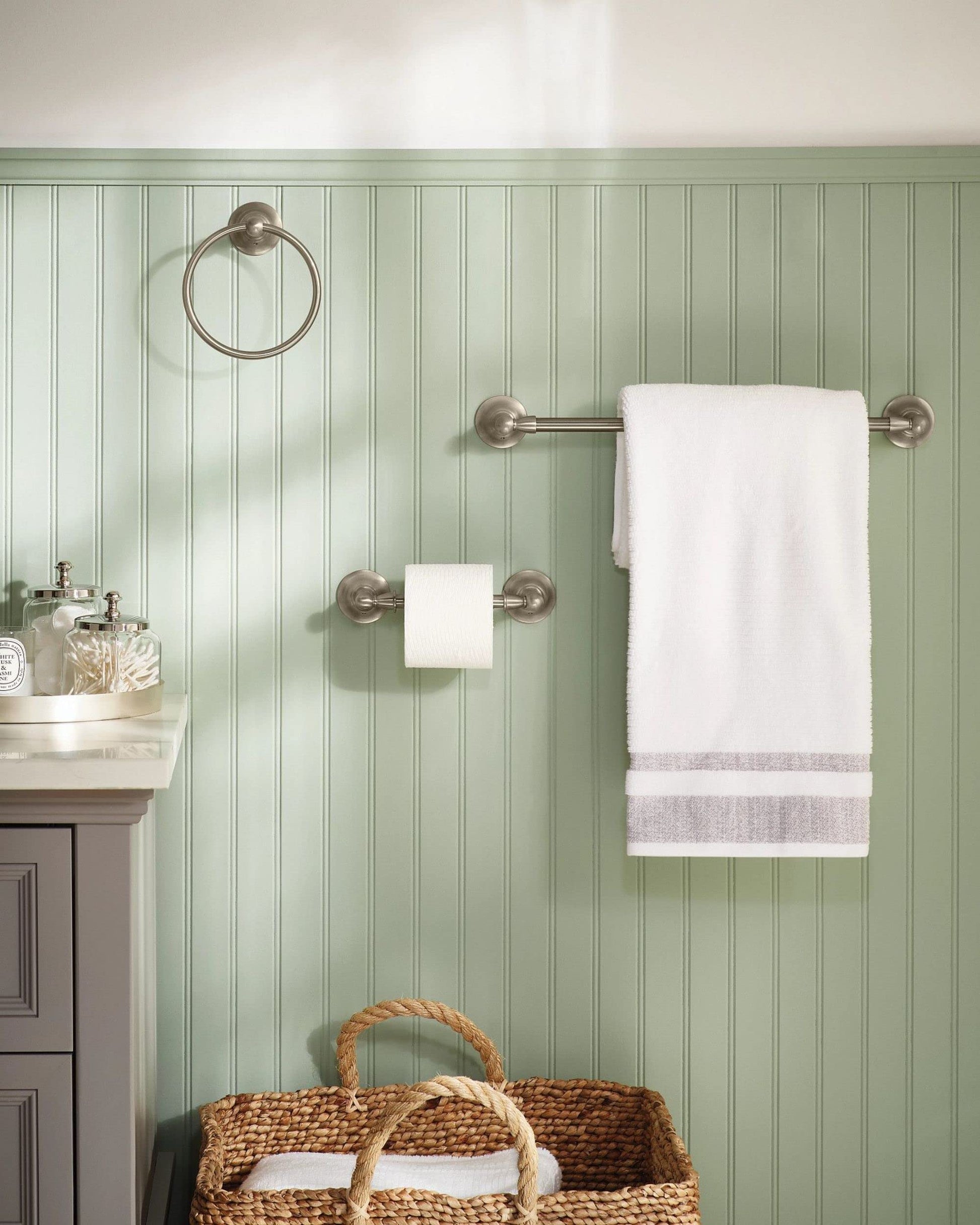 Brushed nickel wall-mount towel ring installed on green paneled bathroom wall above storage basket.