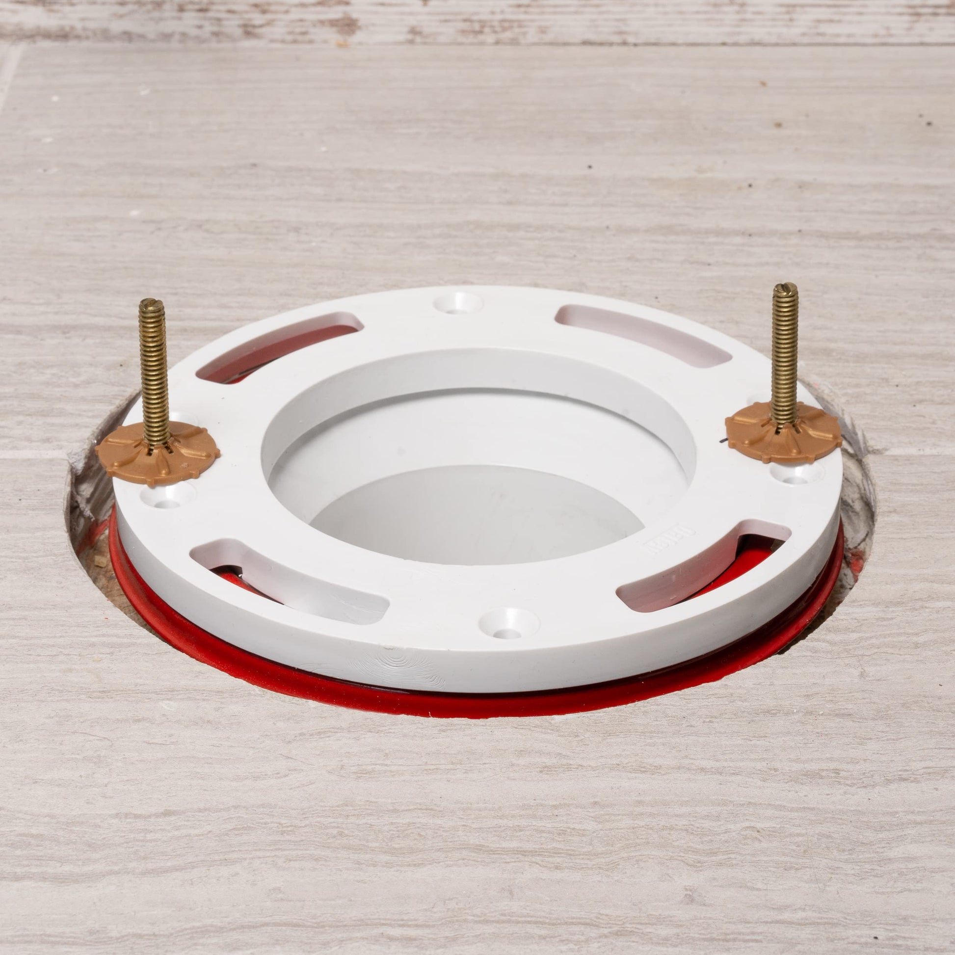 White PVC closet flange spacer with red rubber gasket, brass bolts, and central opening.