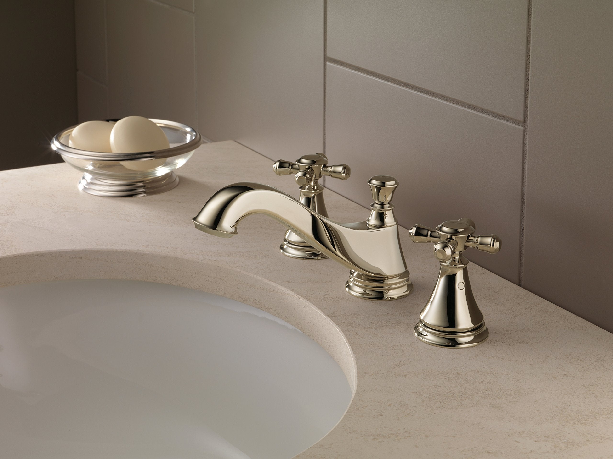 Polished nickel three-piece bathroom faucet set with cross handles and curved spout mounted on beige countertop.