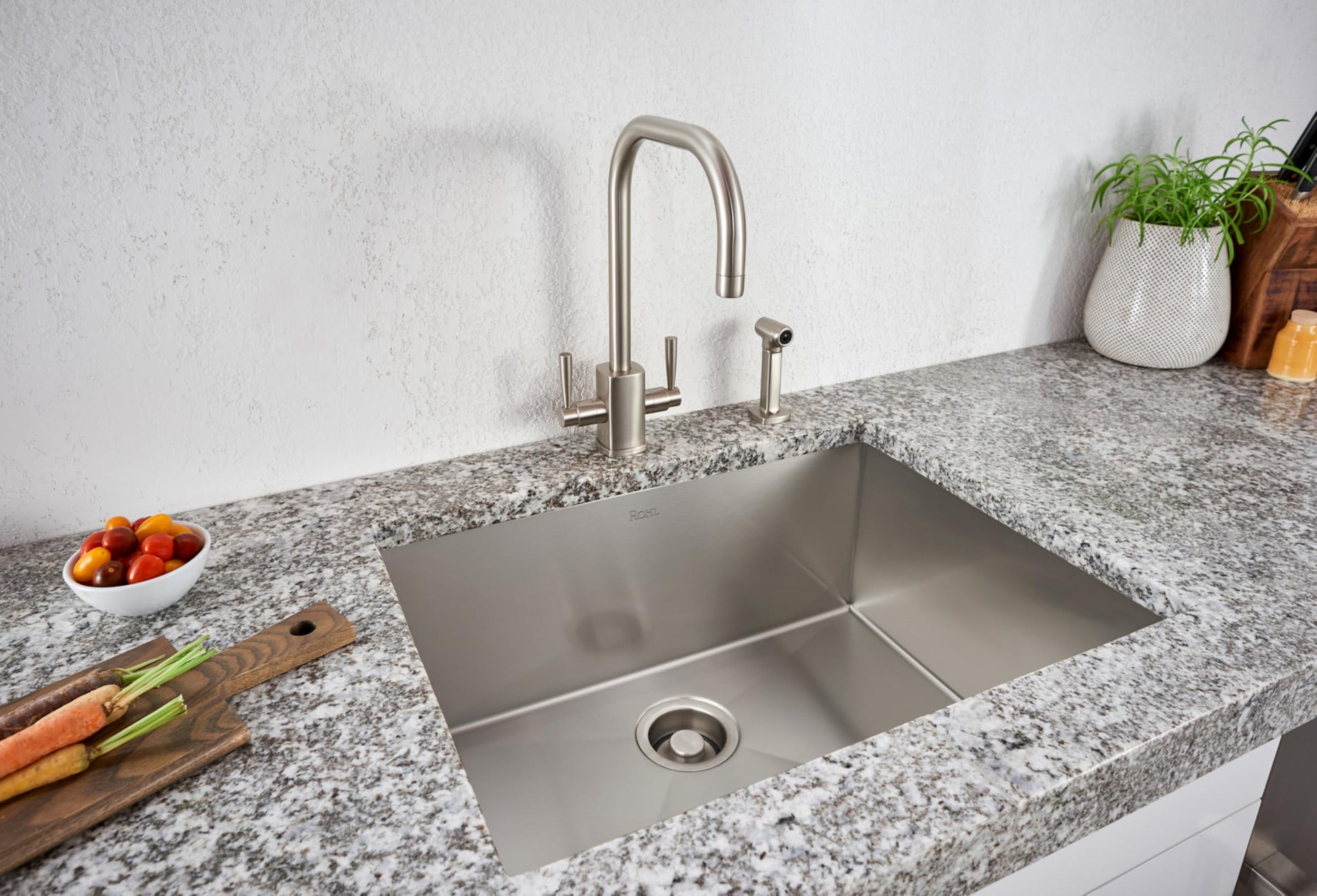 Brushed stainless steel single bowl kitchen sink installed in granite countertop with matching faucet and spray.