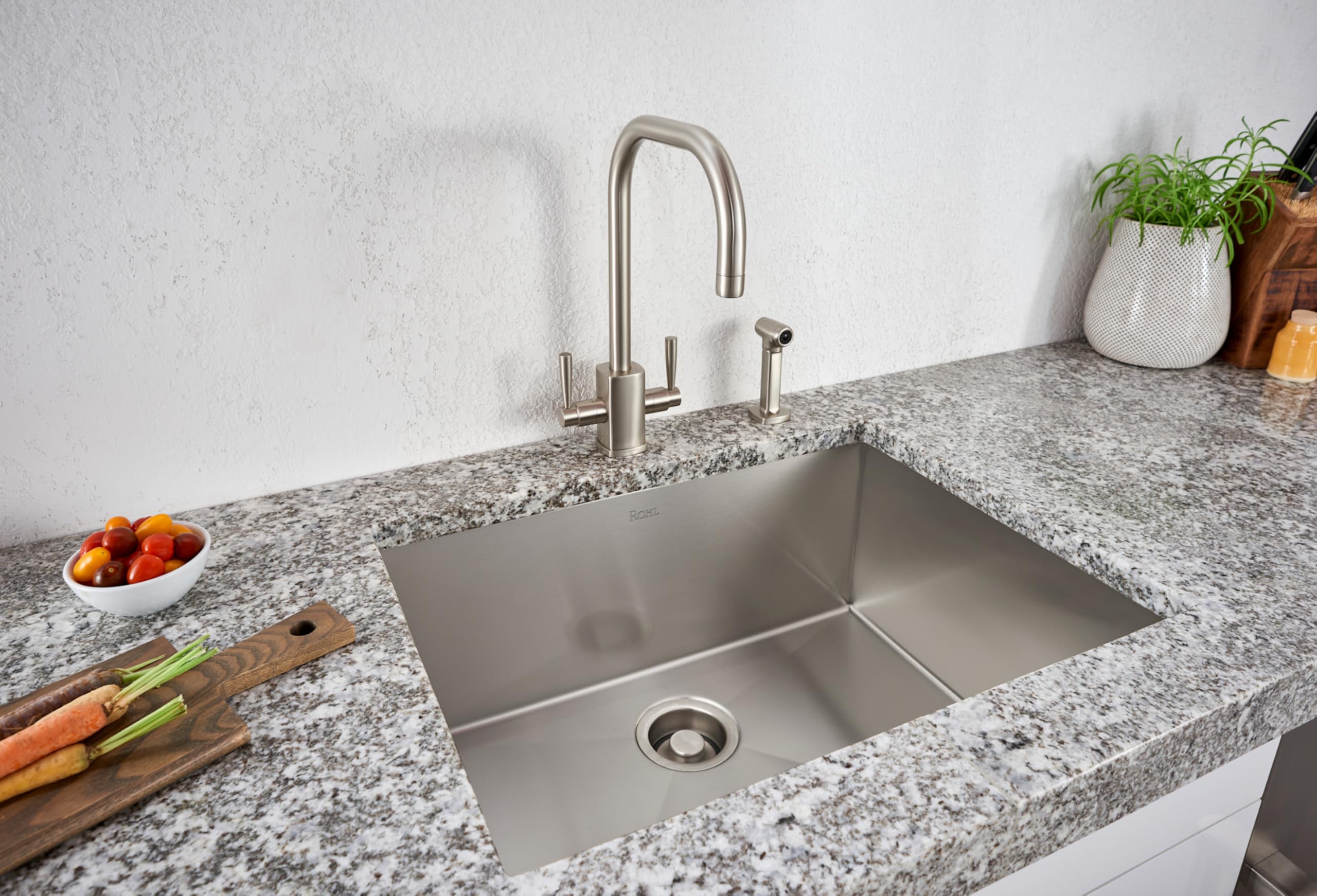 Brushed stainless steel single bowl kitchen sink installed in granite countertop with matching faucet and spray.