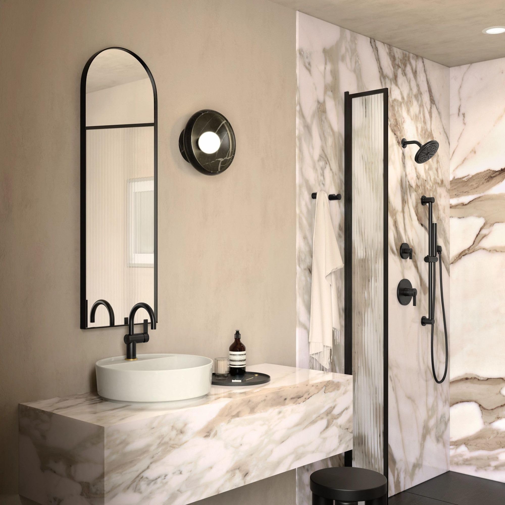 Matte black single-handle transfer valve trim with circular escutcheon, mounted on marble bathroom wall above white vessel si