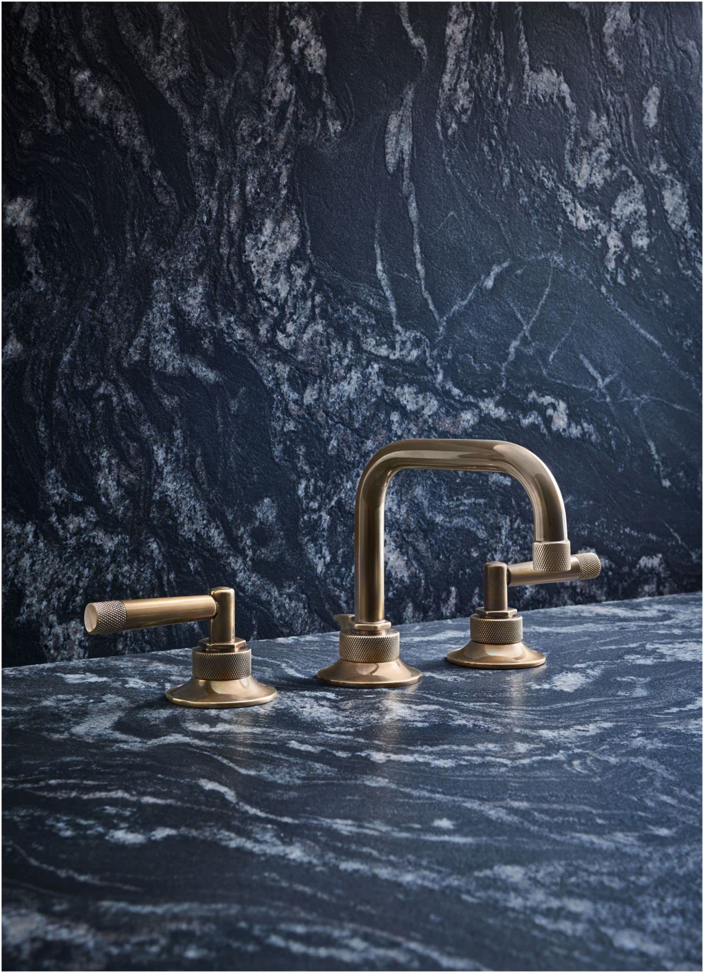 Polished nickel widespread lavatory faucet with U-shaped spout and knurled lever handles on dark marble countertop.